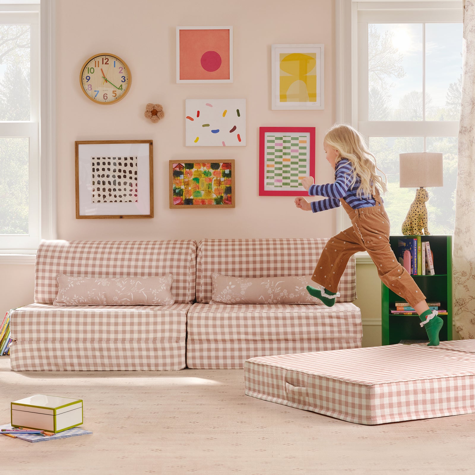 Child jumping on a checkered ottoman in a room with a checkered sofa and colorful artwork on the wall.