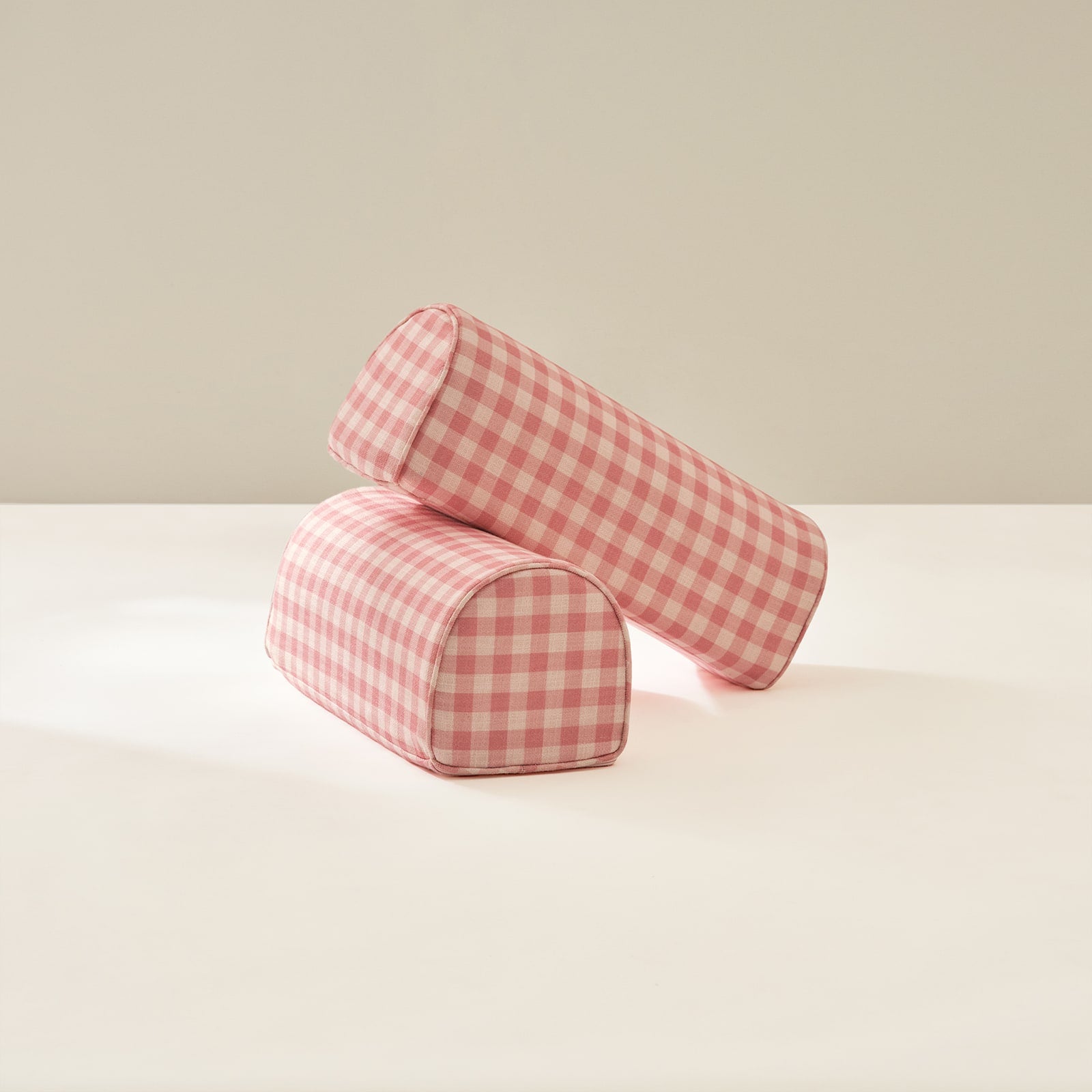 Two pink checkered cylindrical armrests on a light beige background