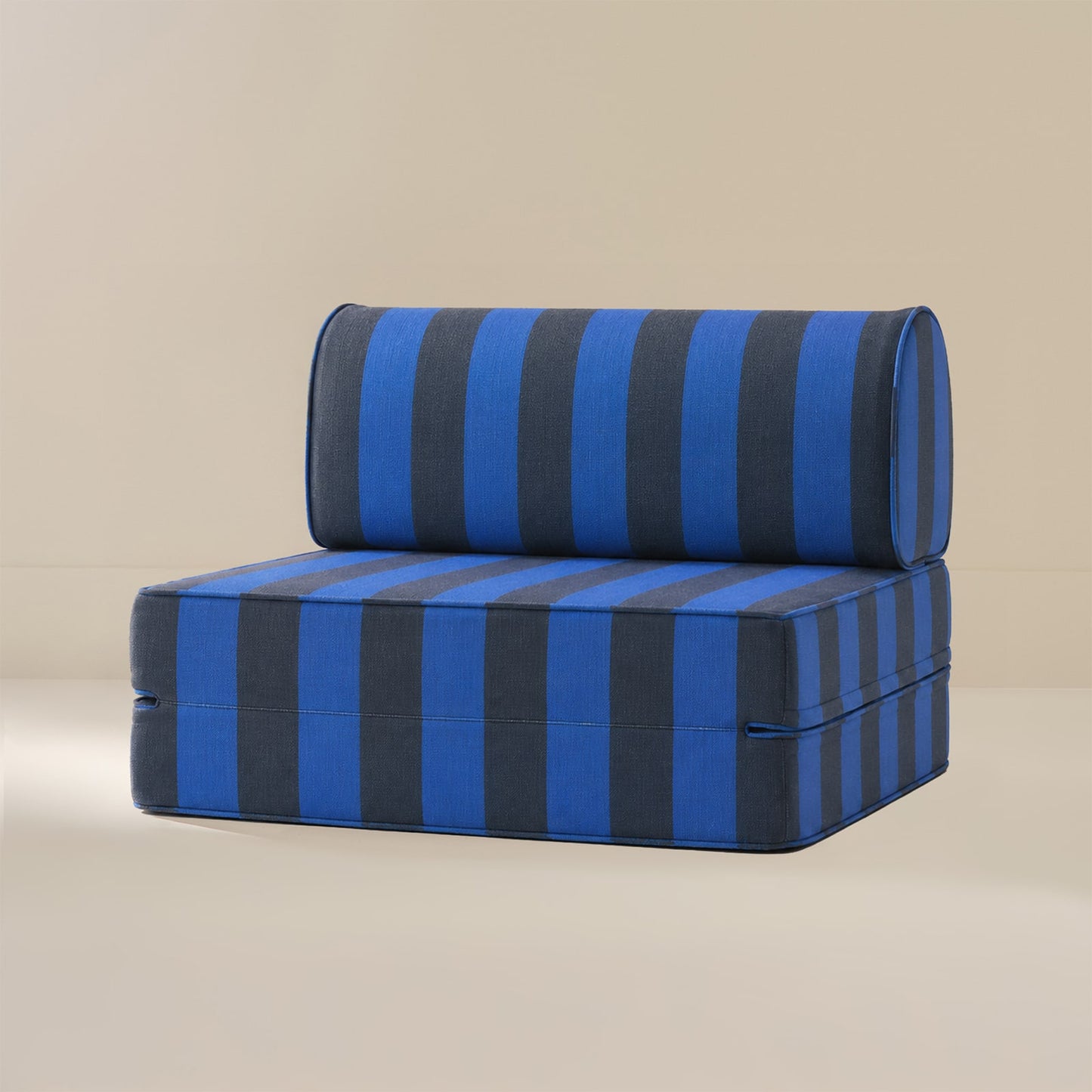 A rectangular upholstered cushion or small chair pad with a matching cylindrical backrest, featuring bold vertical blue and dark charcoal stripes, set against a plain beige studio background.