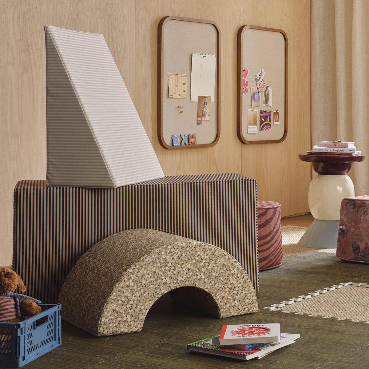 A brown striped arch block topped with a cream striped wedge, with a tan floral arch in front, in a playroom with wood-paneled walls.