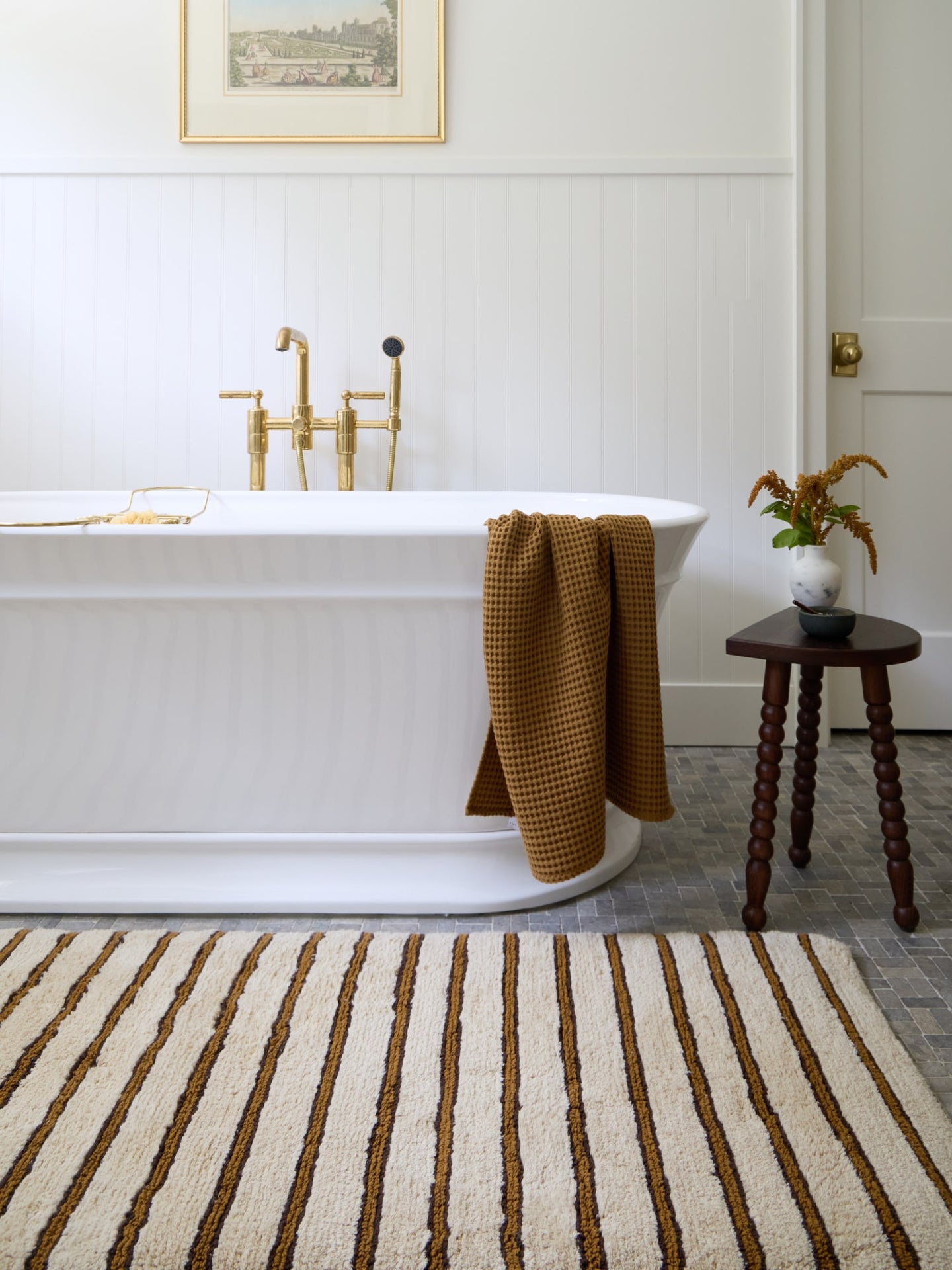 Bathroom with a freestanding bathtub, striped rug, and wooden stool.