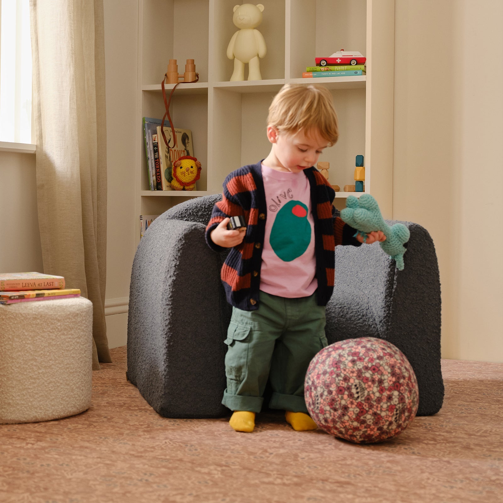 Child playing with a ball and toy in a room with a bean bag chair and shelves.