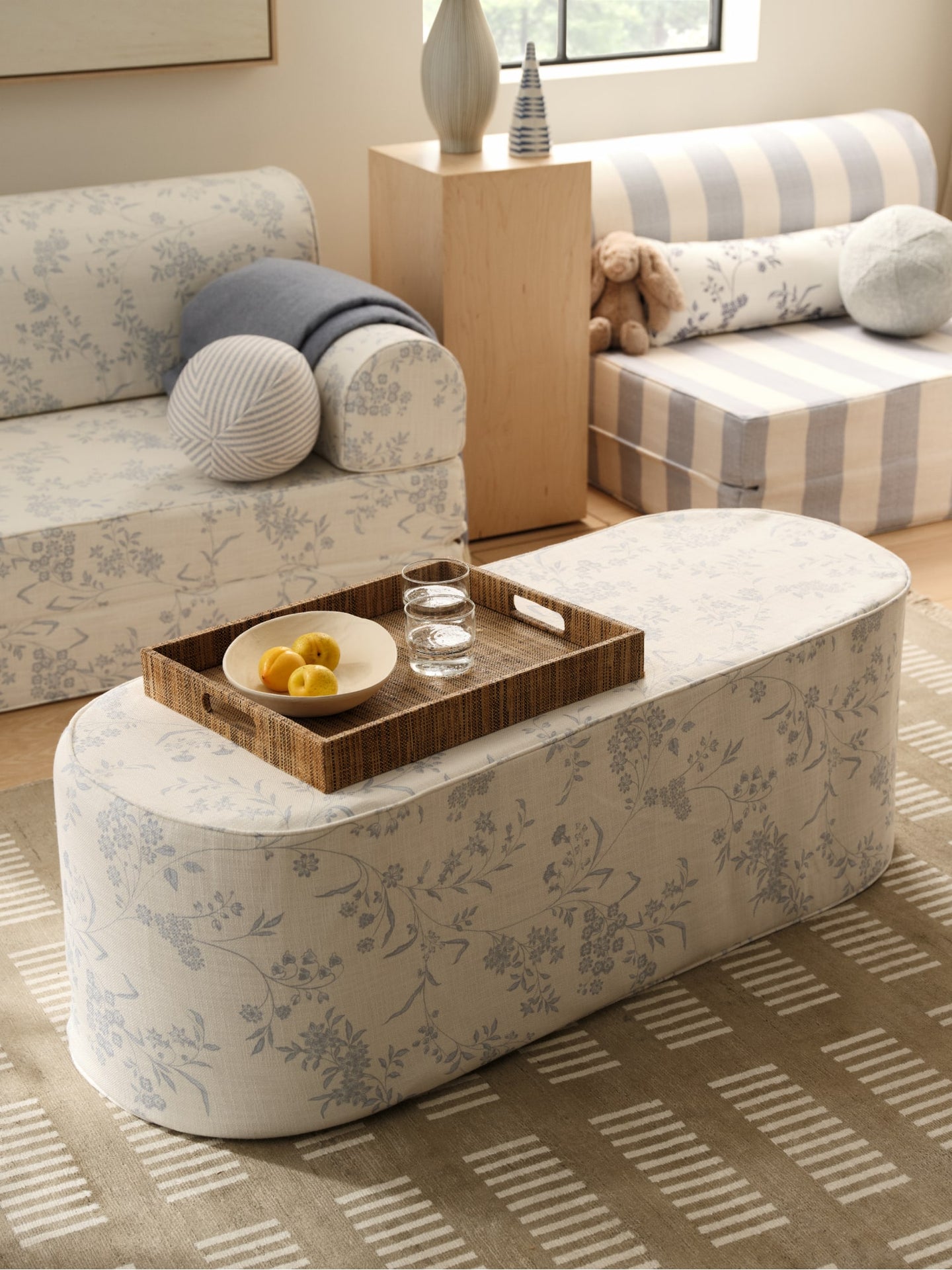 Floral-patterned coffee table with a tray of fruit and water in a living room with floral-patterned and striped play couches and pillows