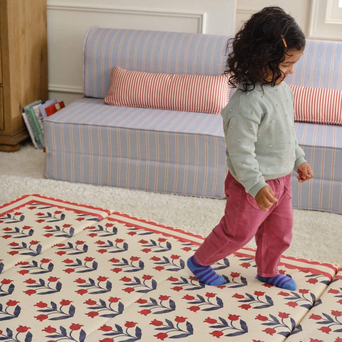 Toddler walking across the Delilah Carnation tumbling mat with a scalloped red border