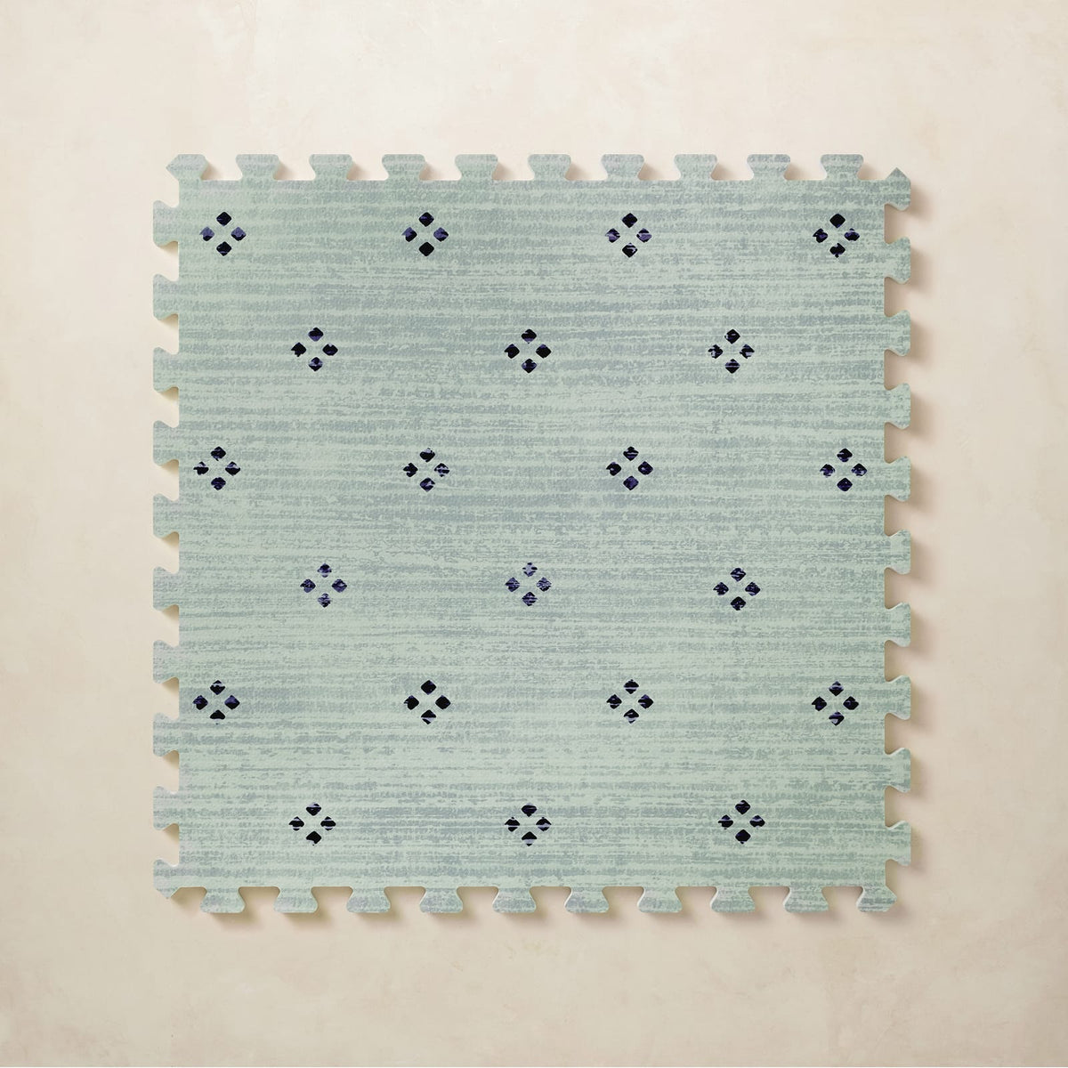 A square interlocking foam play mat tile in soft seafoam with a navy diamond dot motif, shown from above on a light beige background.
