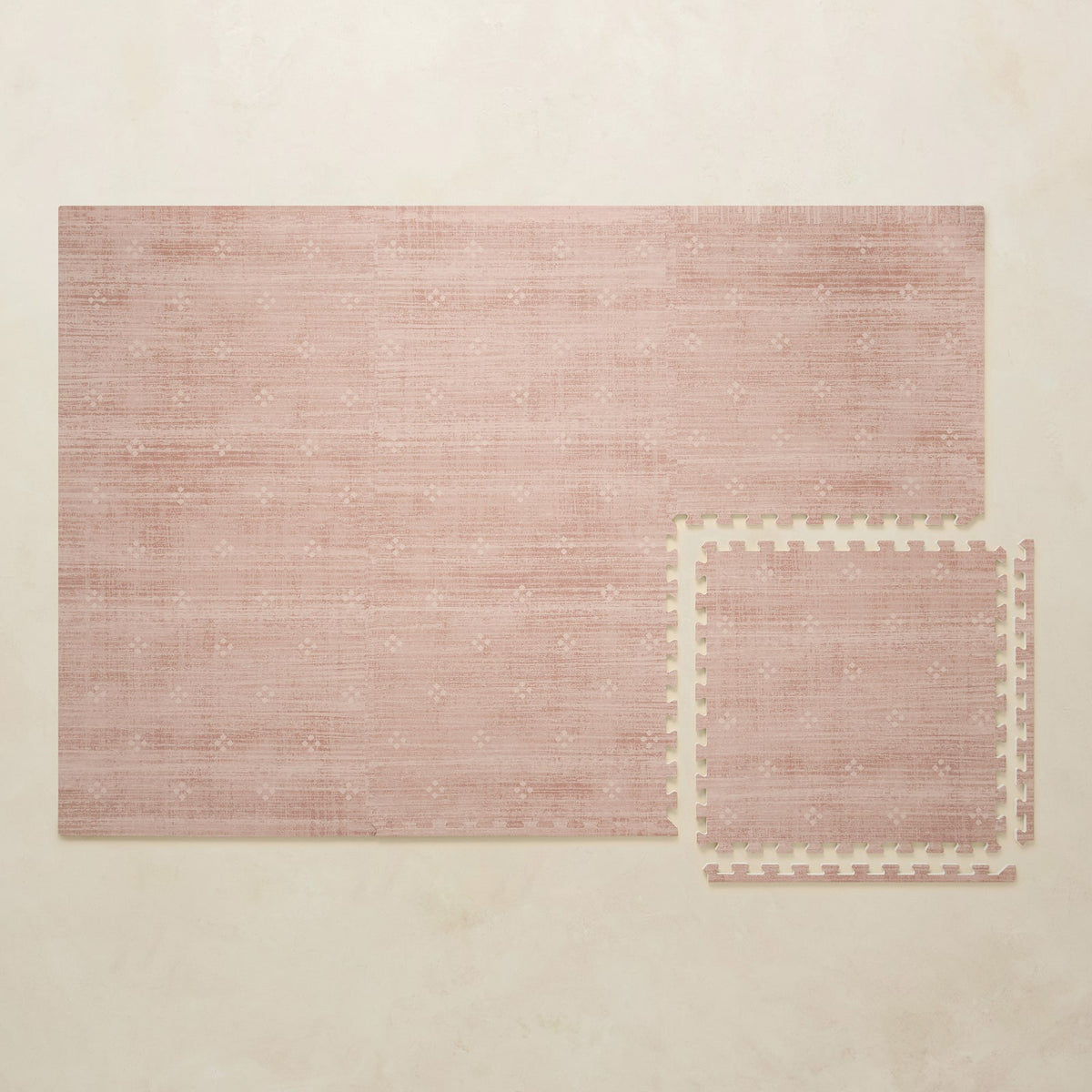 A 4x6 dusty rose foam play mat shown beside a single interlocking tile to compare sizes, photographed from above on a beige background.