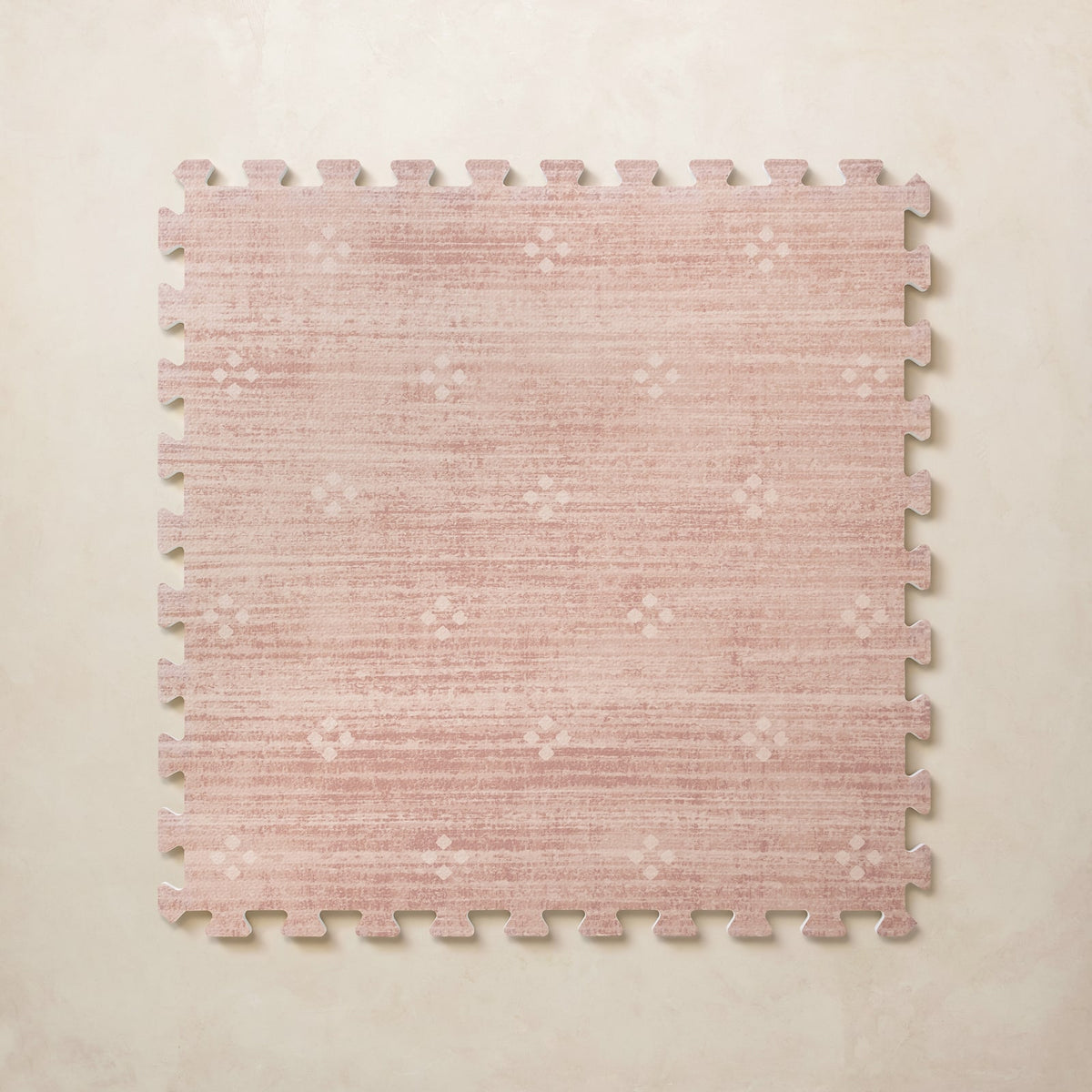 A square interlocking foam play mat tile in dusty rose with a subtle blush diamond dot motif, shown from above on a light beige background.