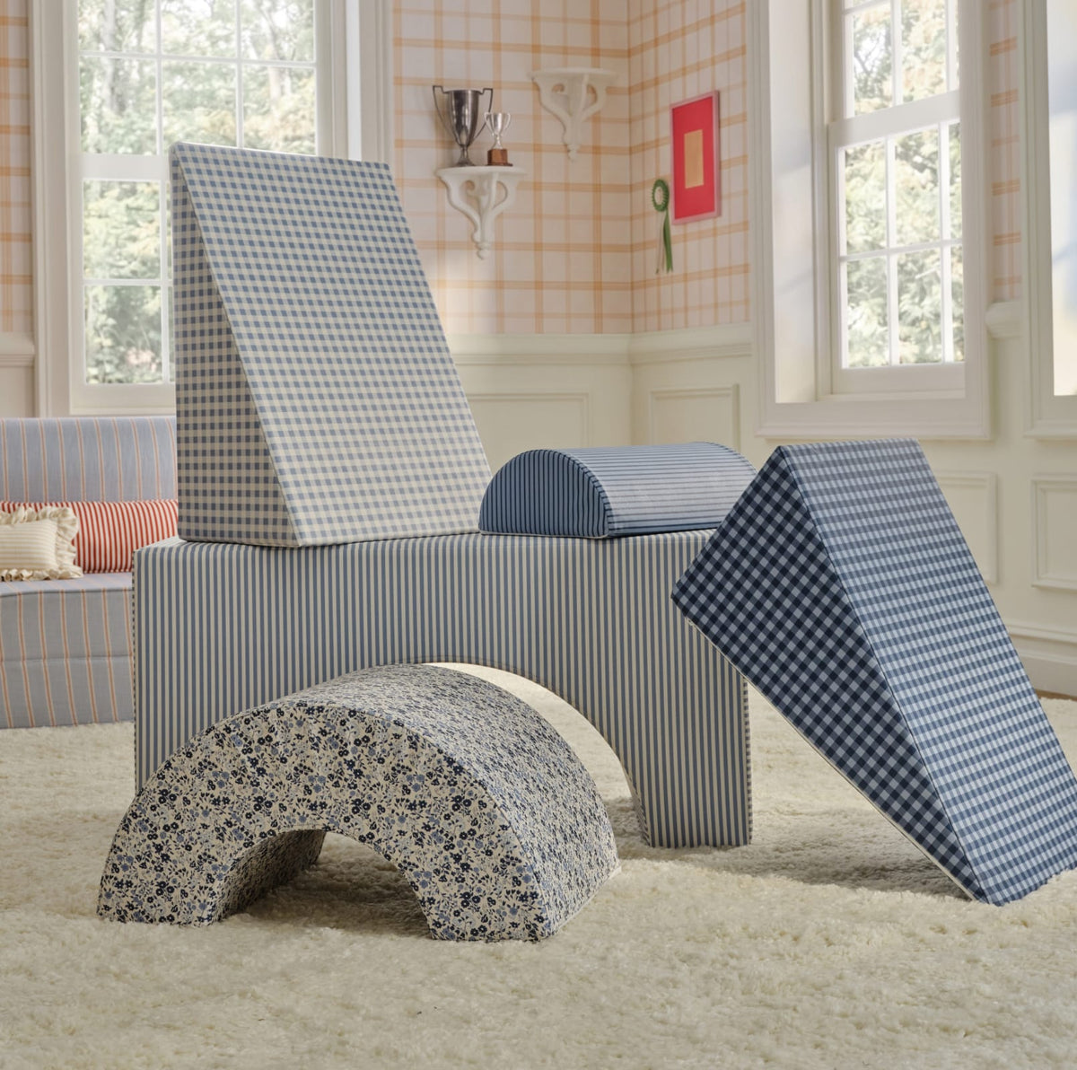 A children's play gym set made from blue-and-white patterned fabric, including a rectangular base, two triangular climbing walls, and an arched tunnel, shown in a bright nursery room.