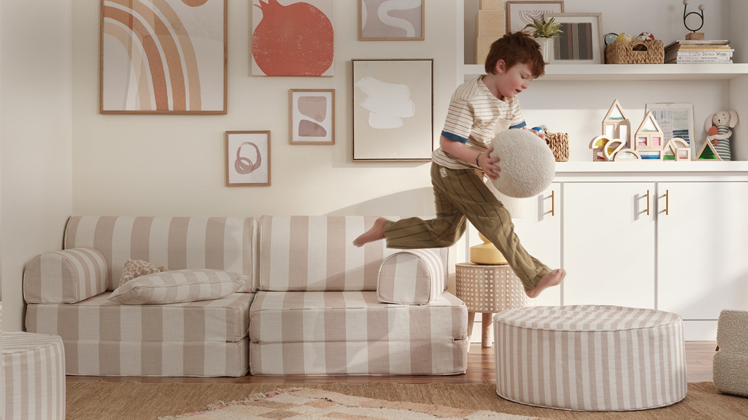 Child jumping on a striped ottoman in a living room with decor elements.