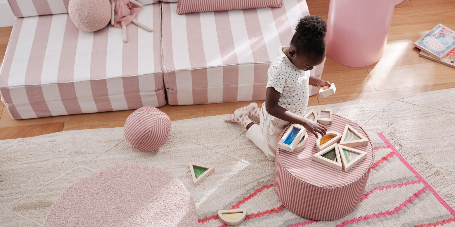 Child playing with geometric shapes on a striped ottoman in a living room.