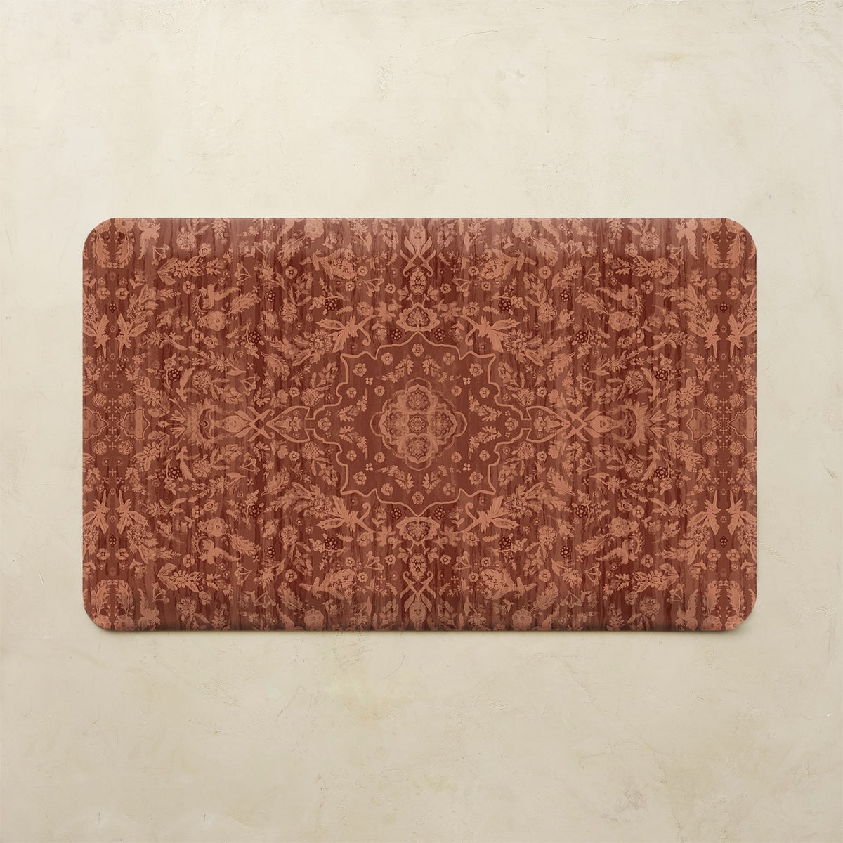 A rectangular bath mat with rounded corners featuring an intricate, symmetrical damask-style floral pattern in warm rust red and terracotta tones, displayed flat against a light beige textured background.