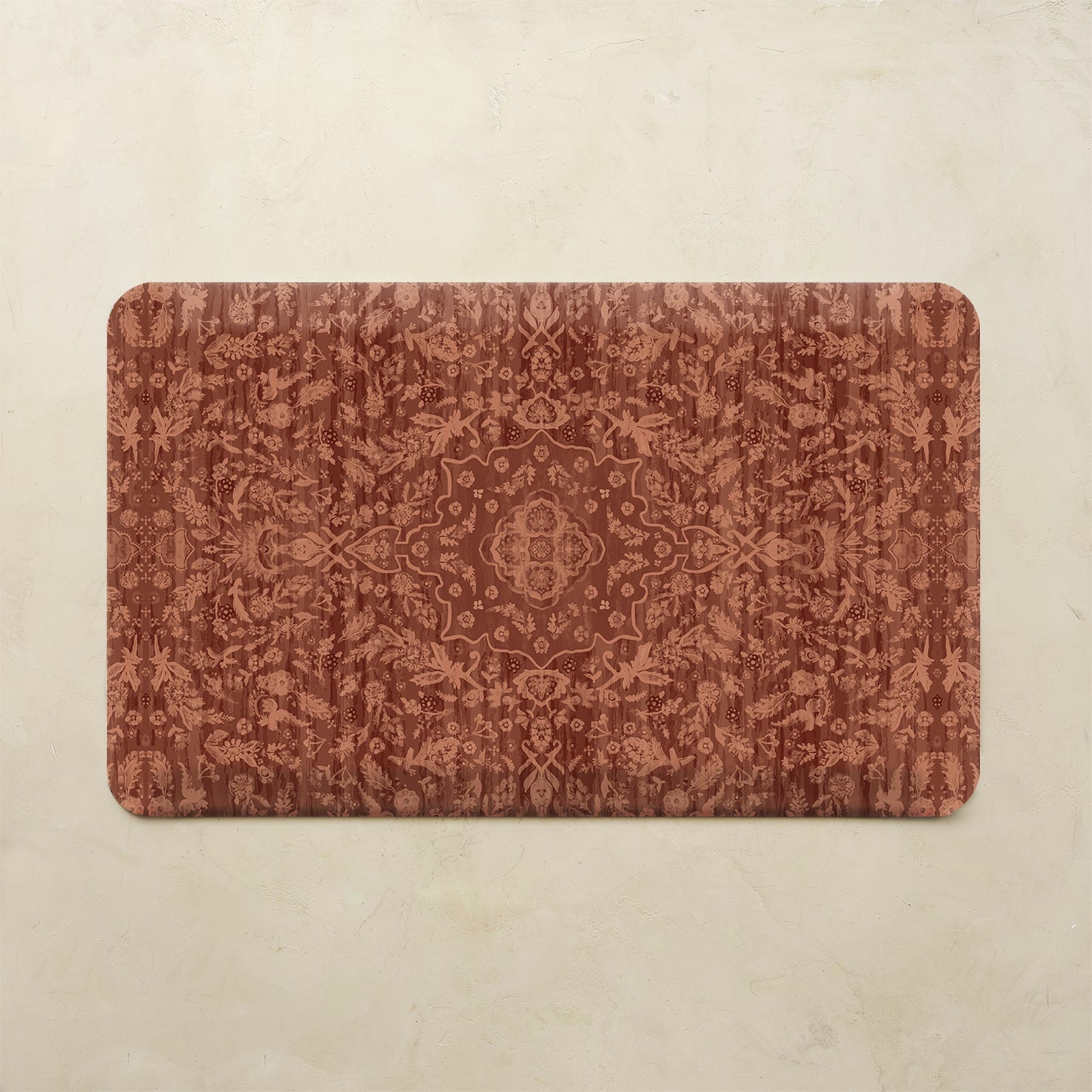 A rectangular bath mat with rounded corners featuring an intricate, symmetrical damask-style floral pattern in warm rust red and terracotta tones, displayed flat against a light beige textured background.