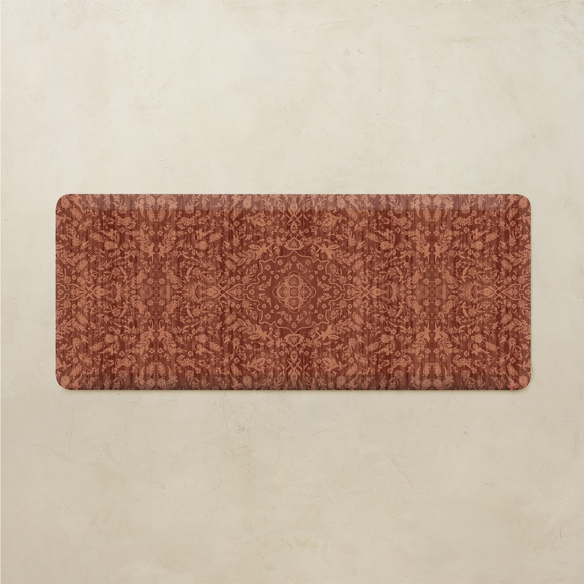 A rectangular floor mat with a distressed, vintage-style ornamental pattern in terracotta and rust brown, displayed flat against a textured beige background.