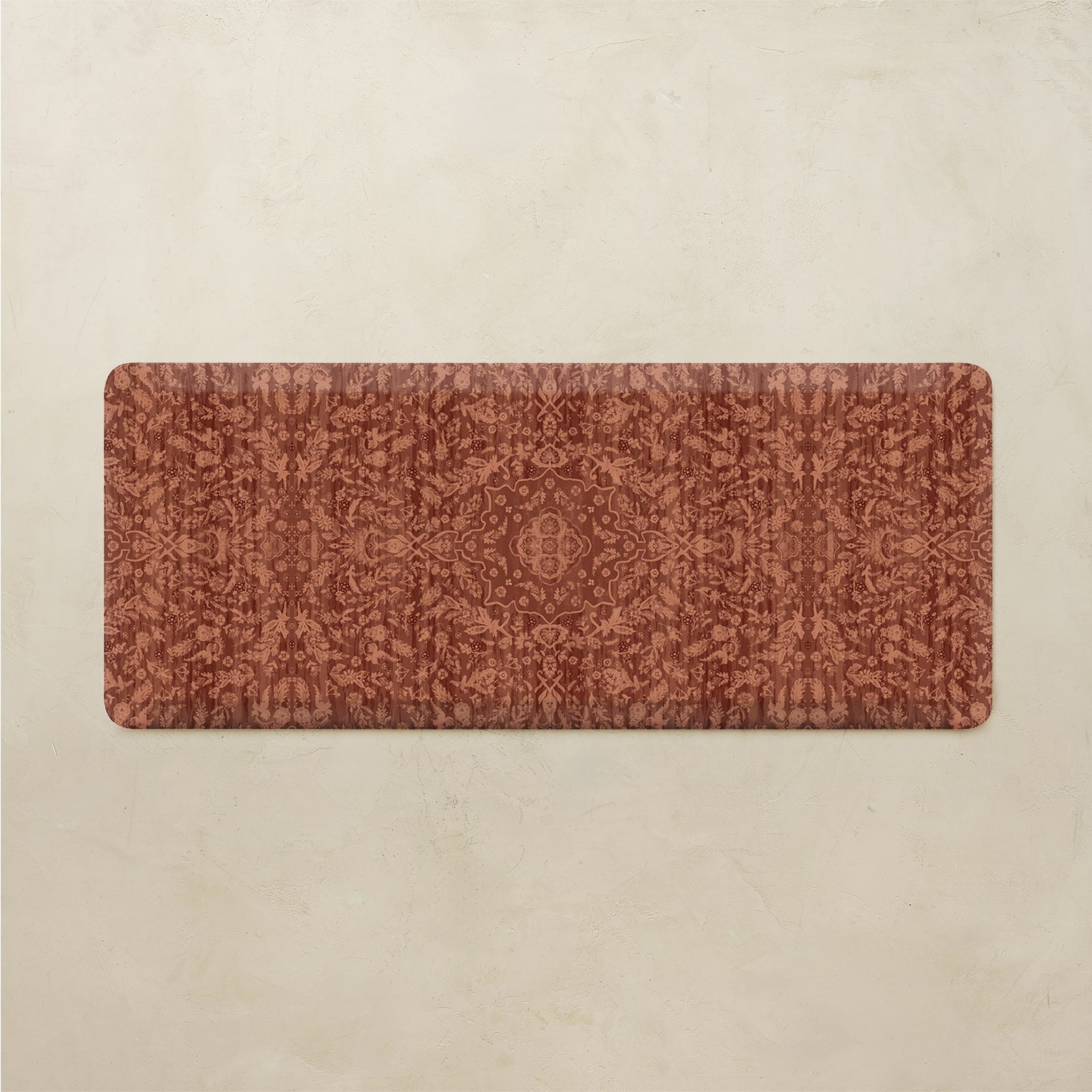 A rectangular floor mat with a distressed, vintage-style ornamental pattern in terracotta and rust brown, displayed flat against a textured beige background.