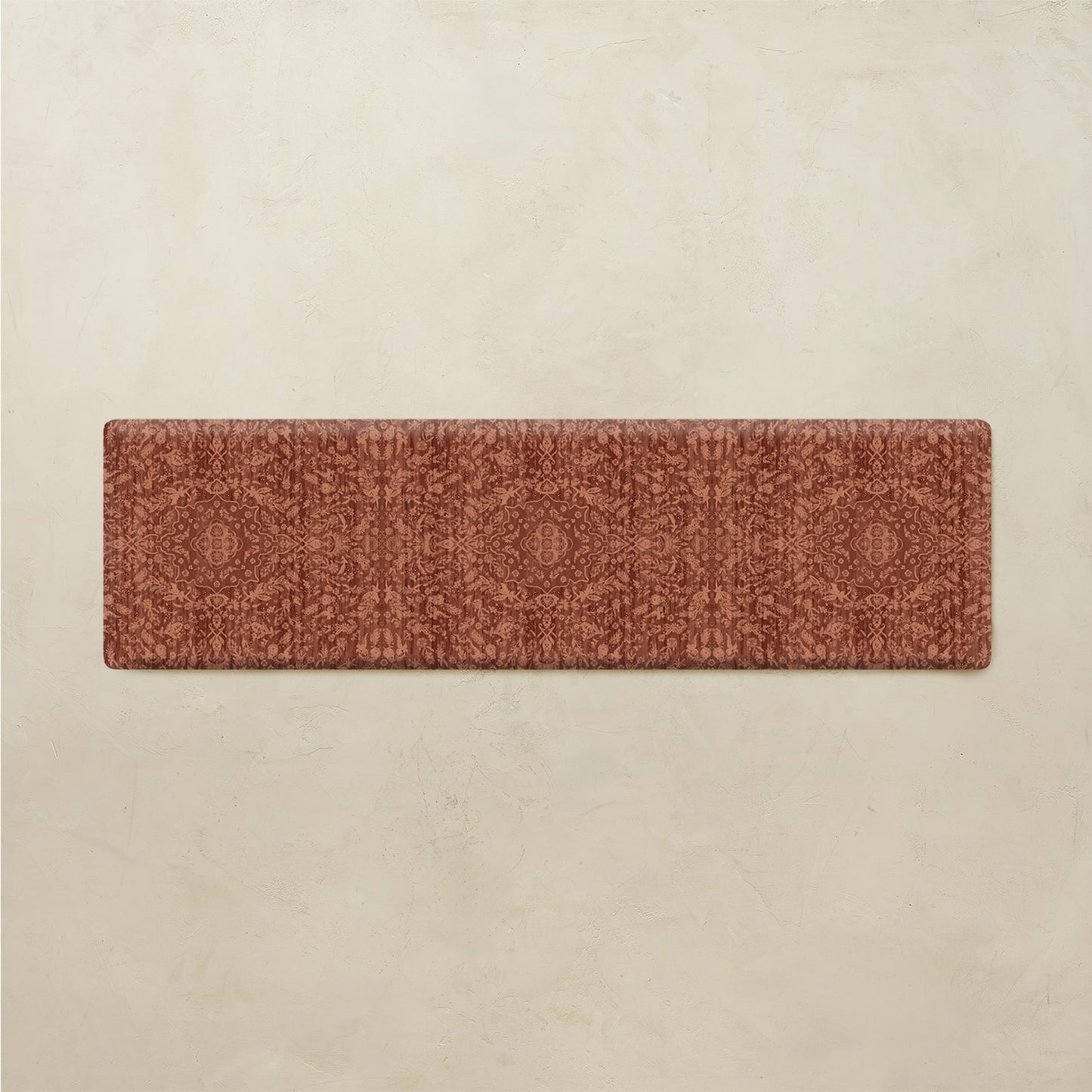A rectangular runner rug with a detailed, repeating geometric and floral pattern in terracotta and rust tones, displayed flat against a textured beige background.