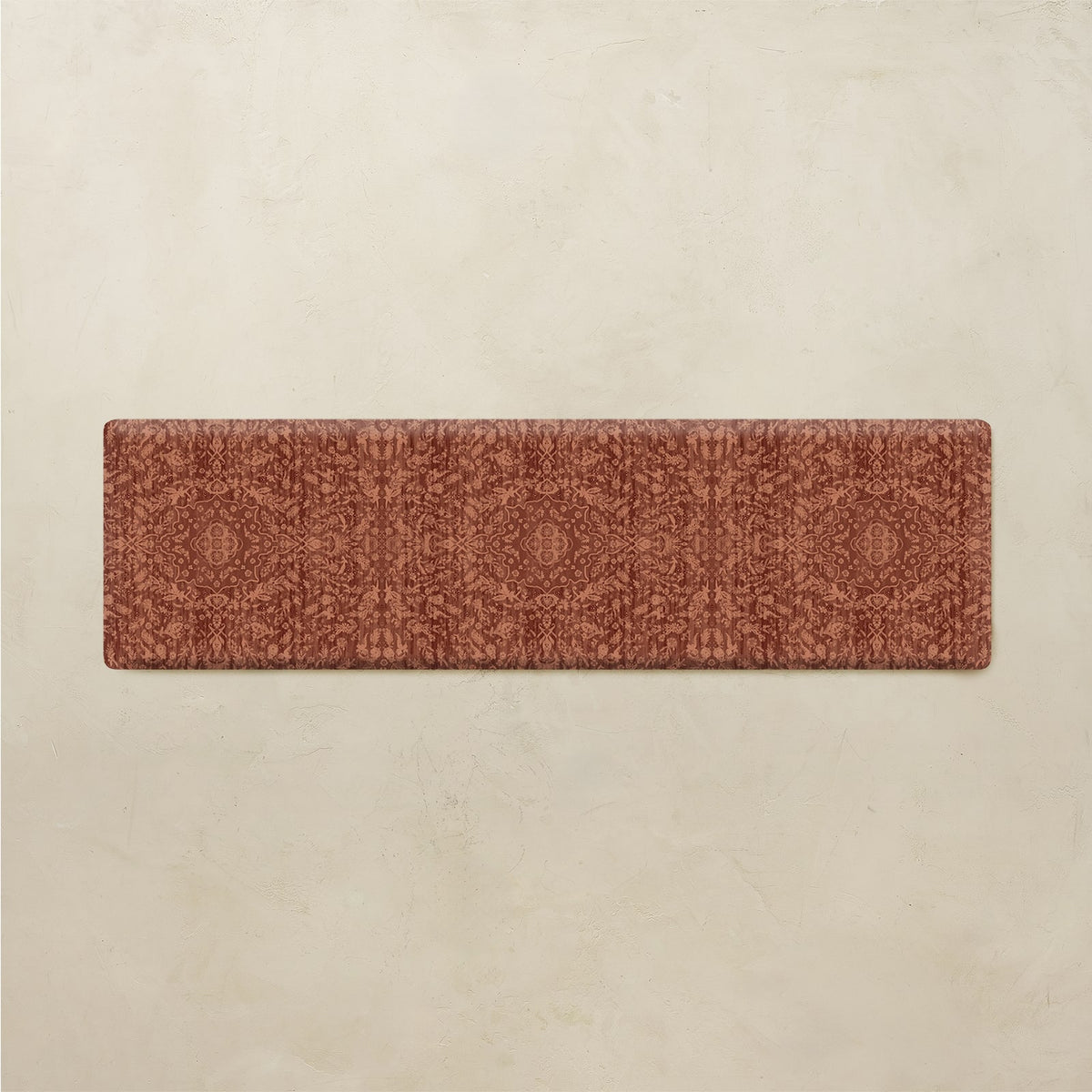 A rectangular runner rug with a detailed, repeating geometric and floral pattern in terracotta and rust tones, displayed flat against a textured beige background.