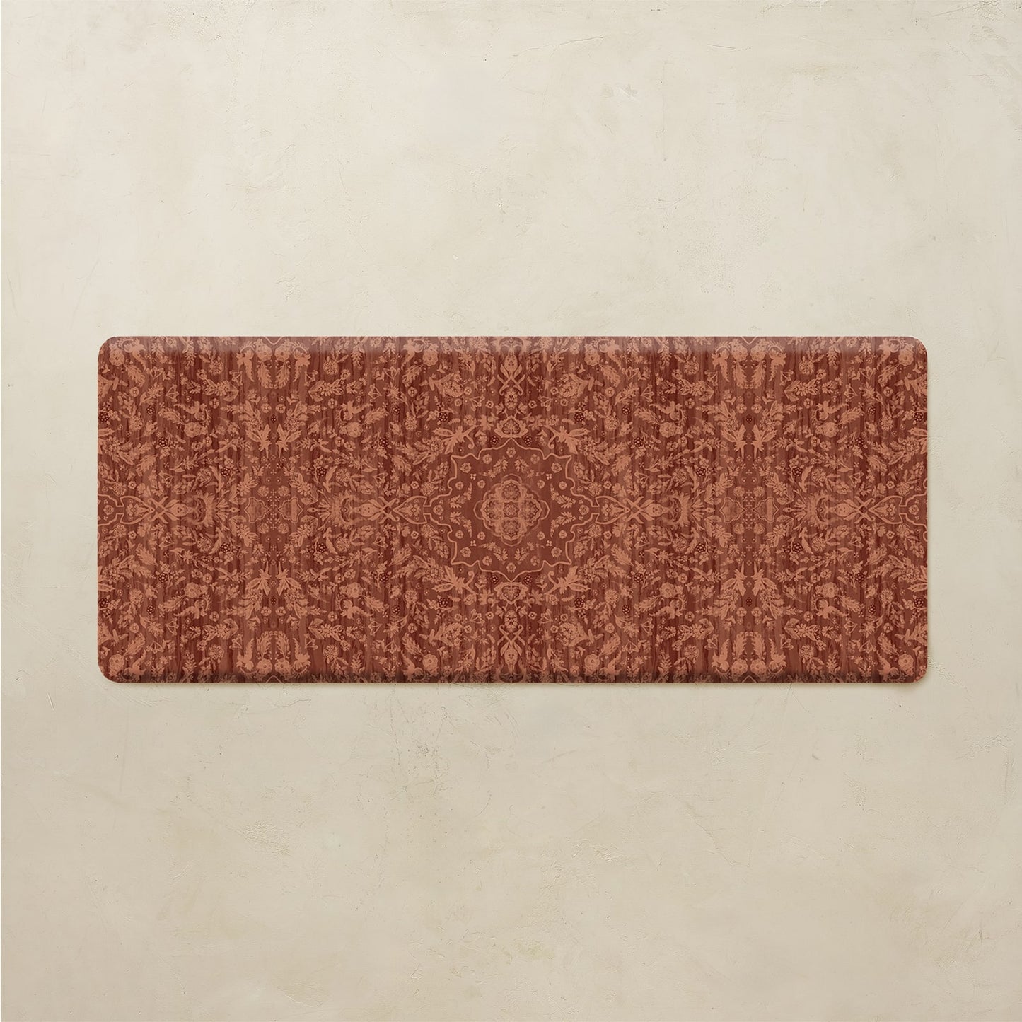 A rectangular floor mat with rounded corners featuring an intricate, symmetrical damask-style pattern in terracotta and rust tones, displayed against a textured beige background.