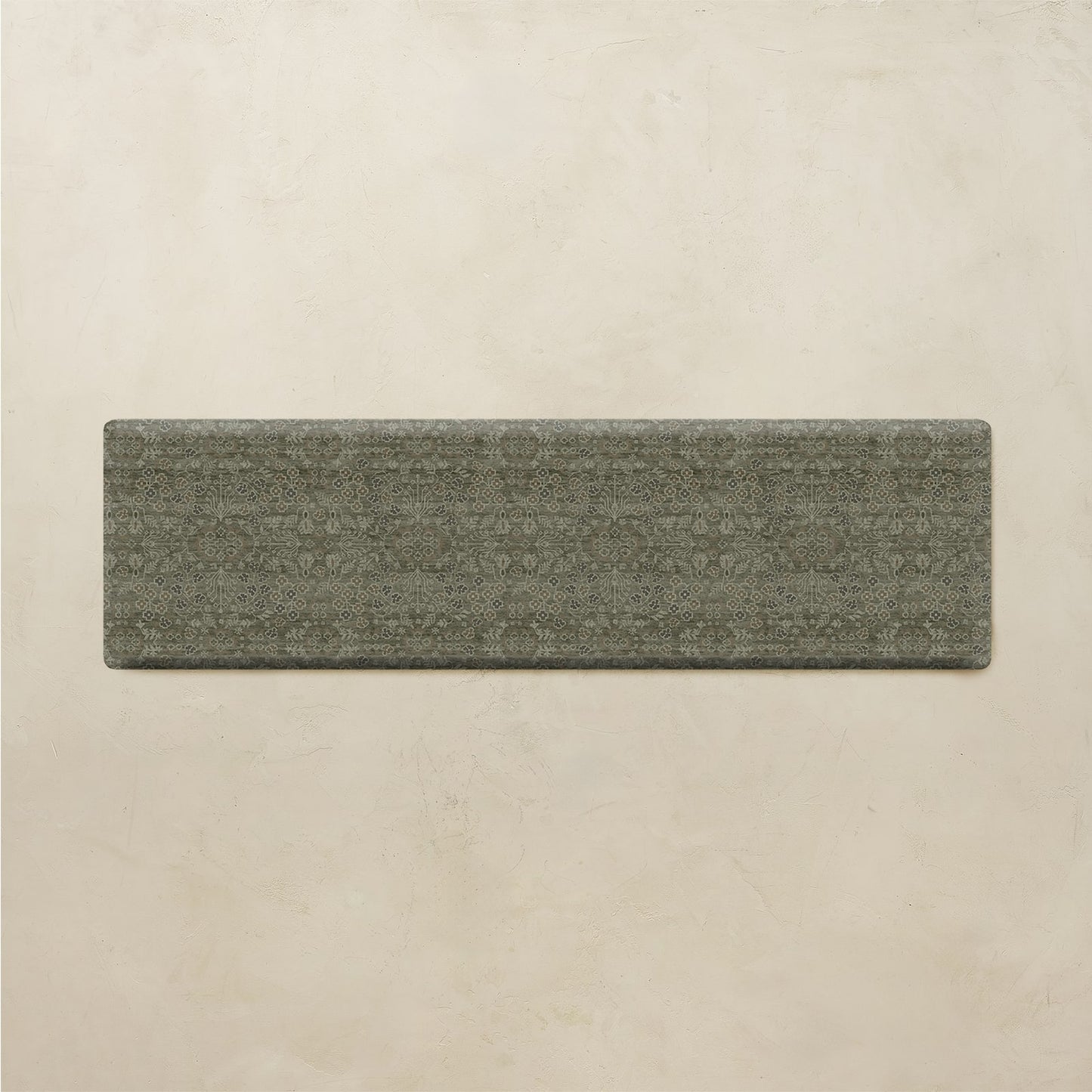 A rectangular gray textured rug with a subtle woven geometric pattern, displayed flat against a warm beige plaster wall.