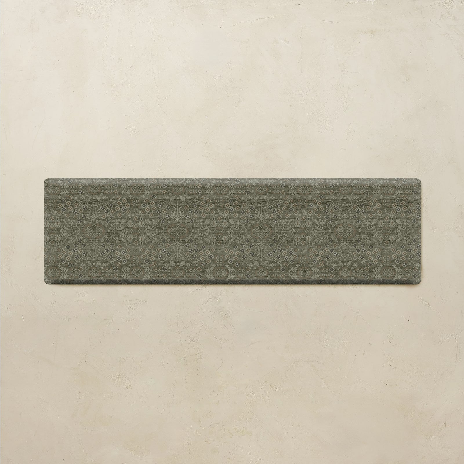 A rectangular gray textured rug with a subtle woven geometric pattern, displayed flat against a warm beige plaster wall.