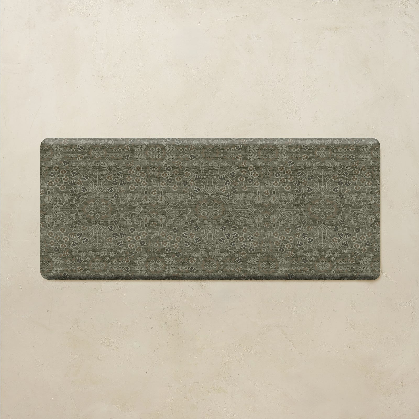 A rectangular floor mat with rounded corners, featuring a distressed, vintage-style ornamental pattern in muted olive green and gray tones, displayed against a textured beige background.
