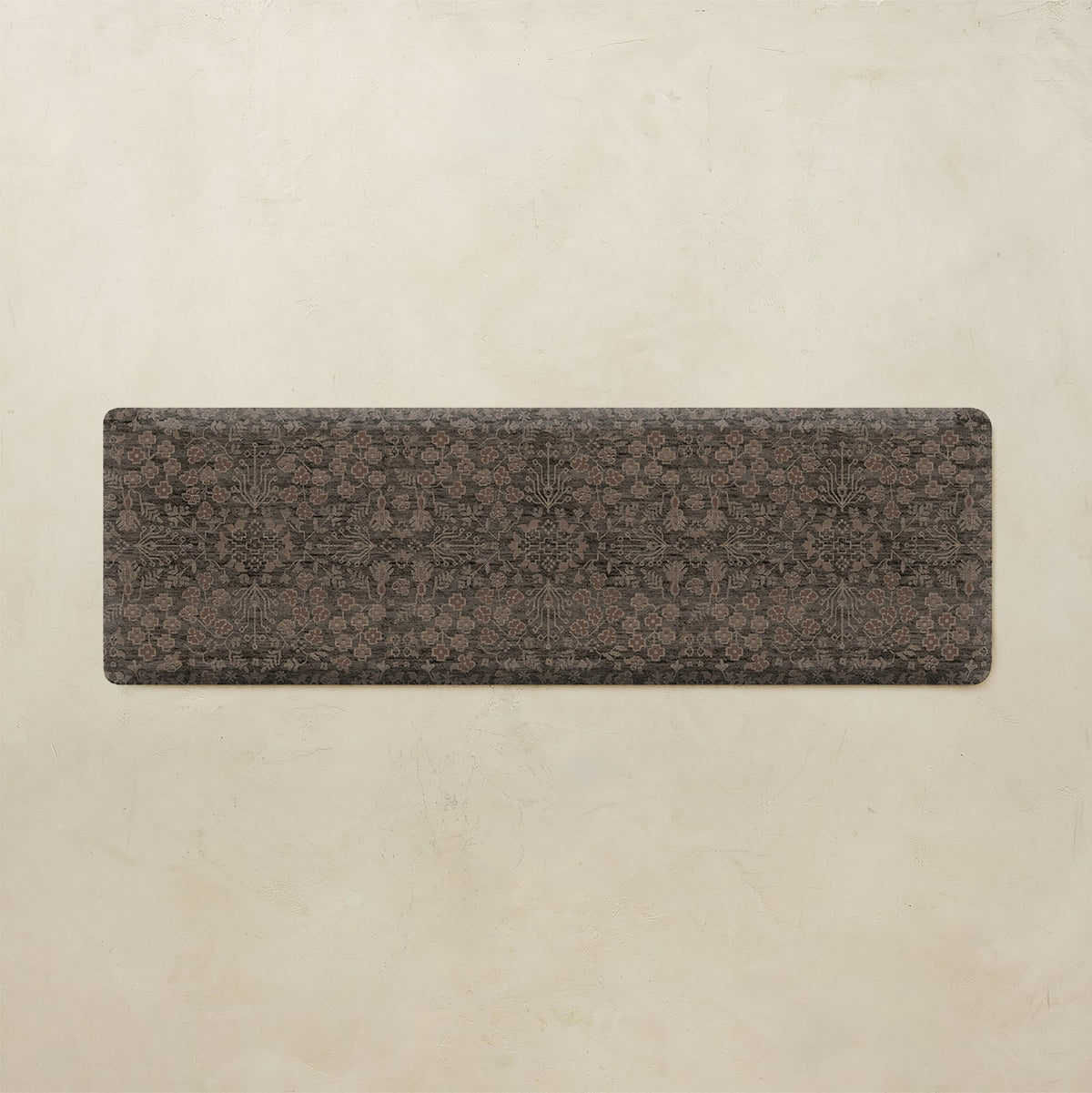 A rectangular yoga mat with a dark brown and black floral pattern, displayed flat against a textured beige background.