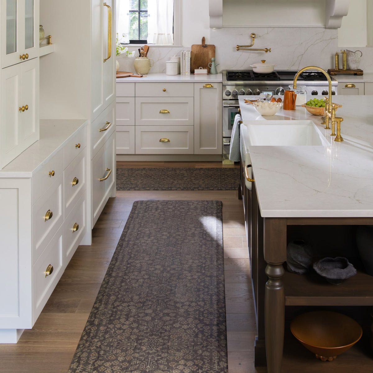 A long, dark gray floral-patterned runner rug is styled in a bright, modern kitchen with white cabinets, a marble island, and gold hardware.