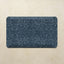 A rectangular bath mat with rounded corners featuring a dark navy blue and slate gray traditional floral pattern, displayed on a textured beige stone surface.