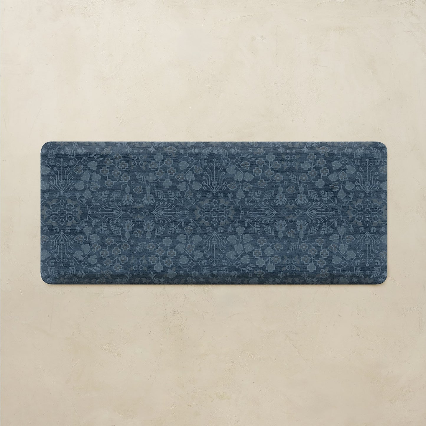 A rectangular blue bath mat with an intricate floral and botanical pattern, displayed flat against a textured beige background.