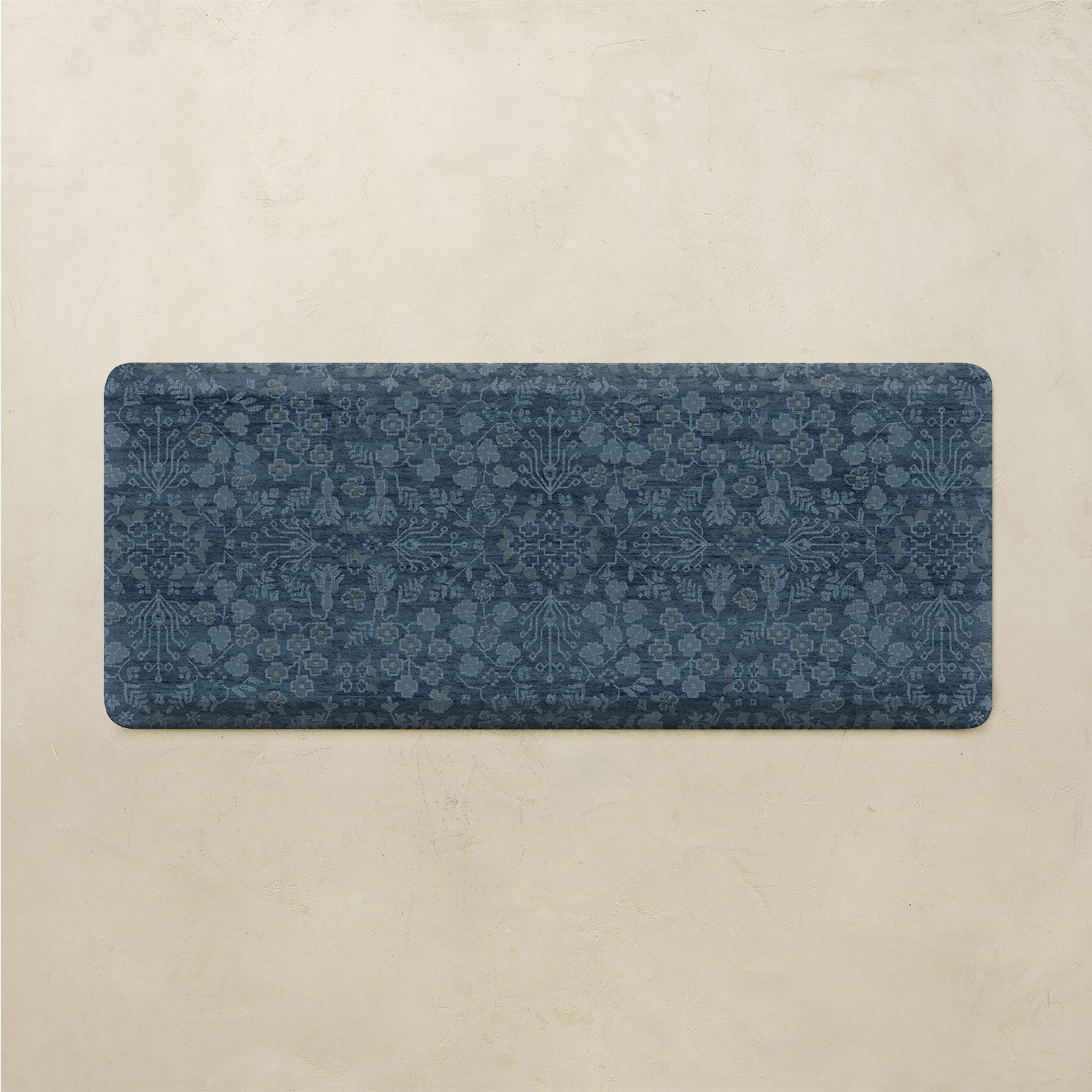 A rectangular blue bath mat with an intricate floral and botanical pattern, displayed flat against a textured beige background.