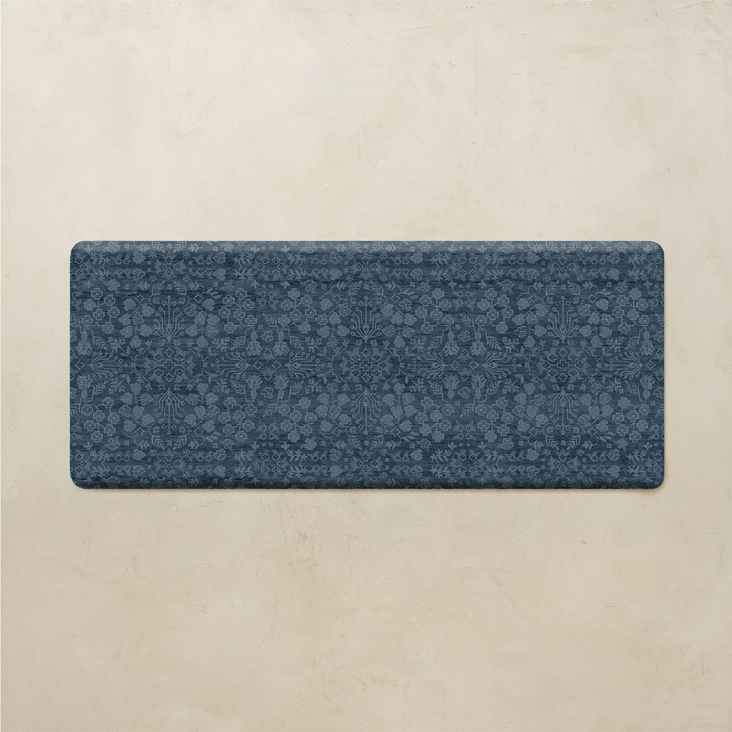 A rectangular blue yoga mat with an intricate floral and geometric pattern, displayed flat against a textured beige background.