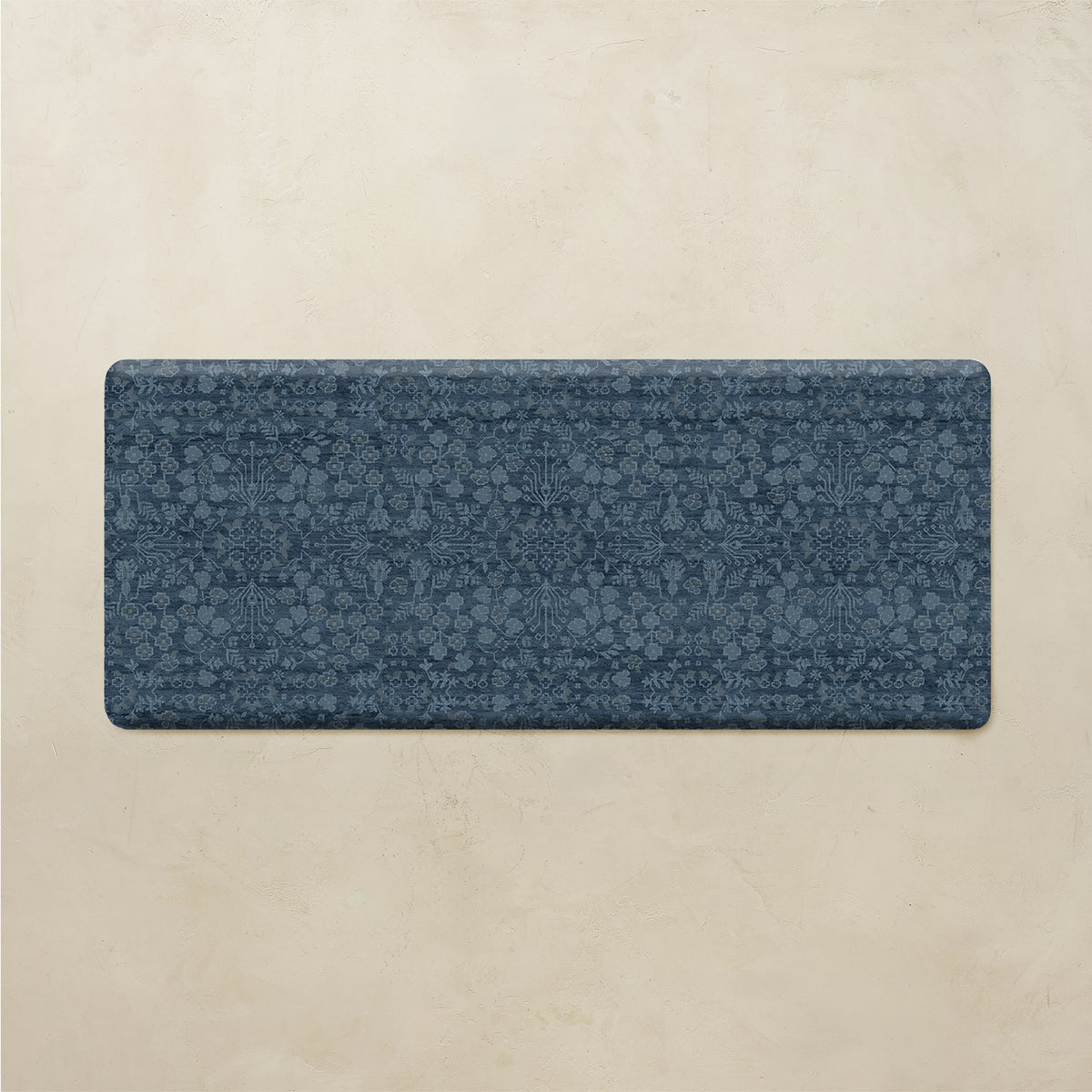 A rectangular blue yoga mat with an intricate floral and geometric pattern, displayed flat against a textured beige background.