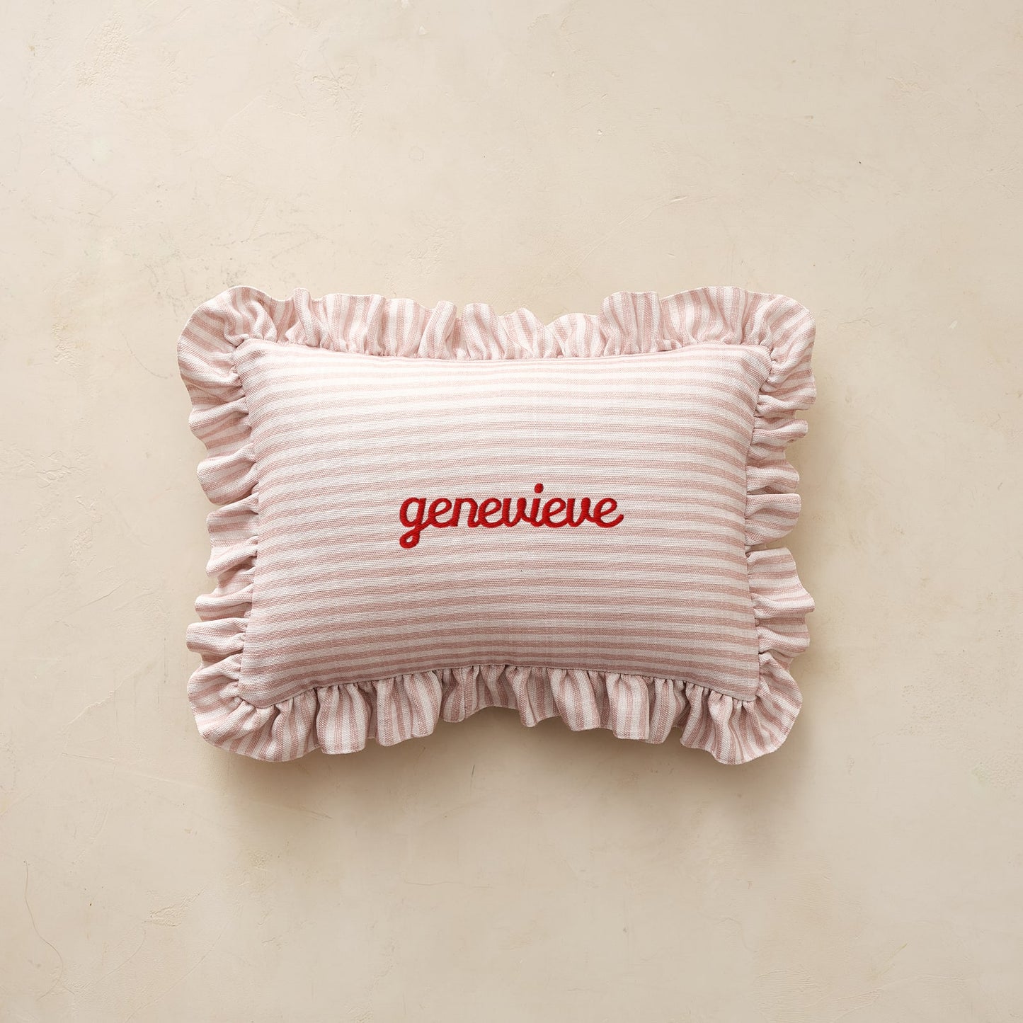 Striped pillow with ruffles and 'genevieve' embroidery on a beige background