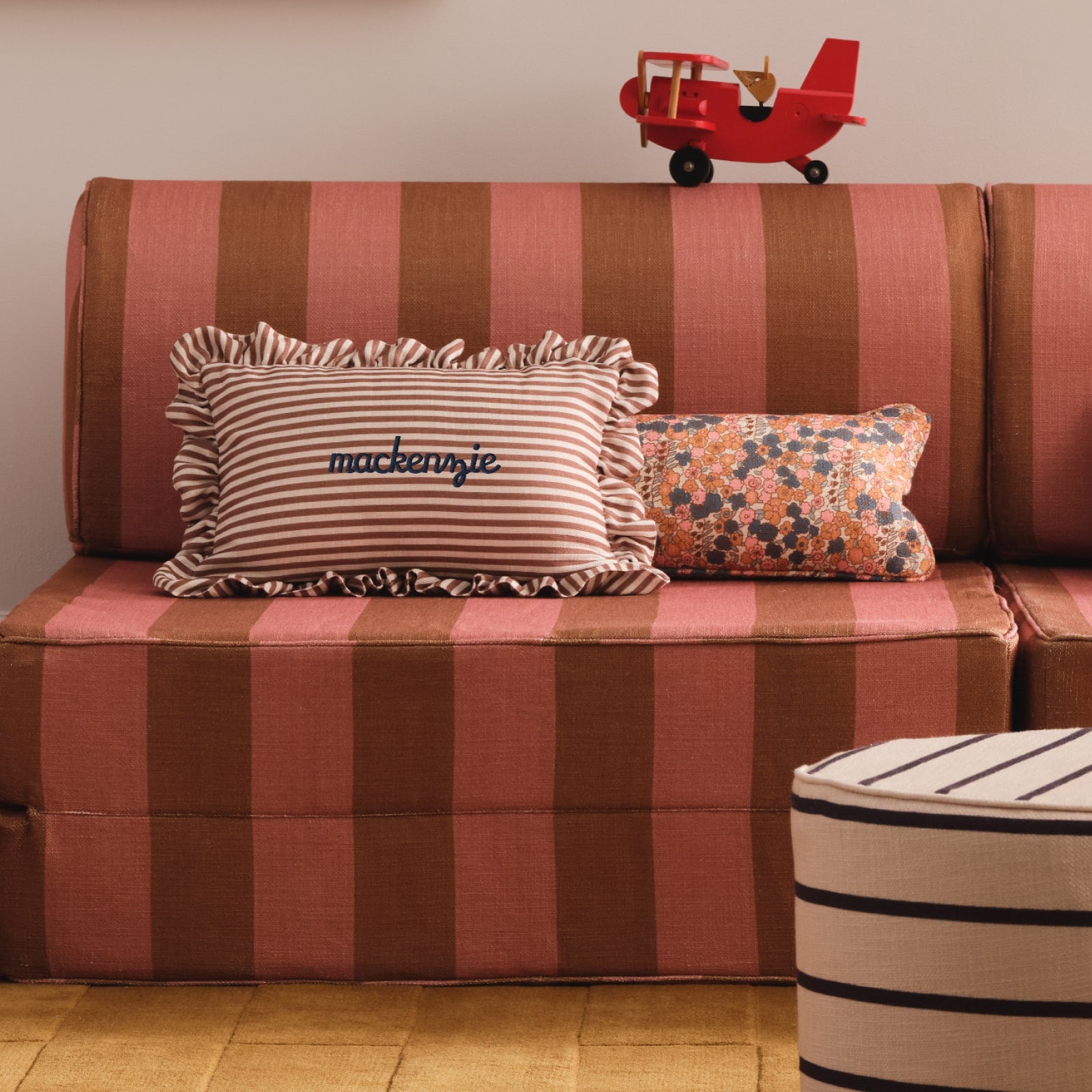Striped sofa with decorative pillows and a red toy airplane on a beige wall background