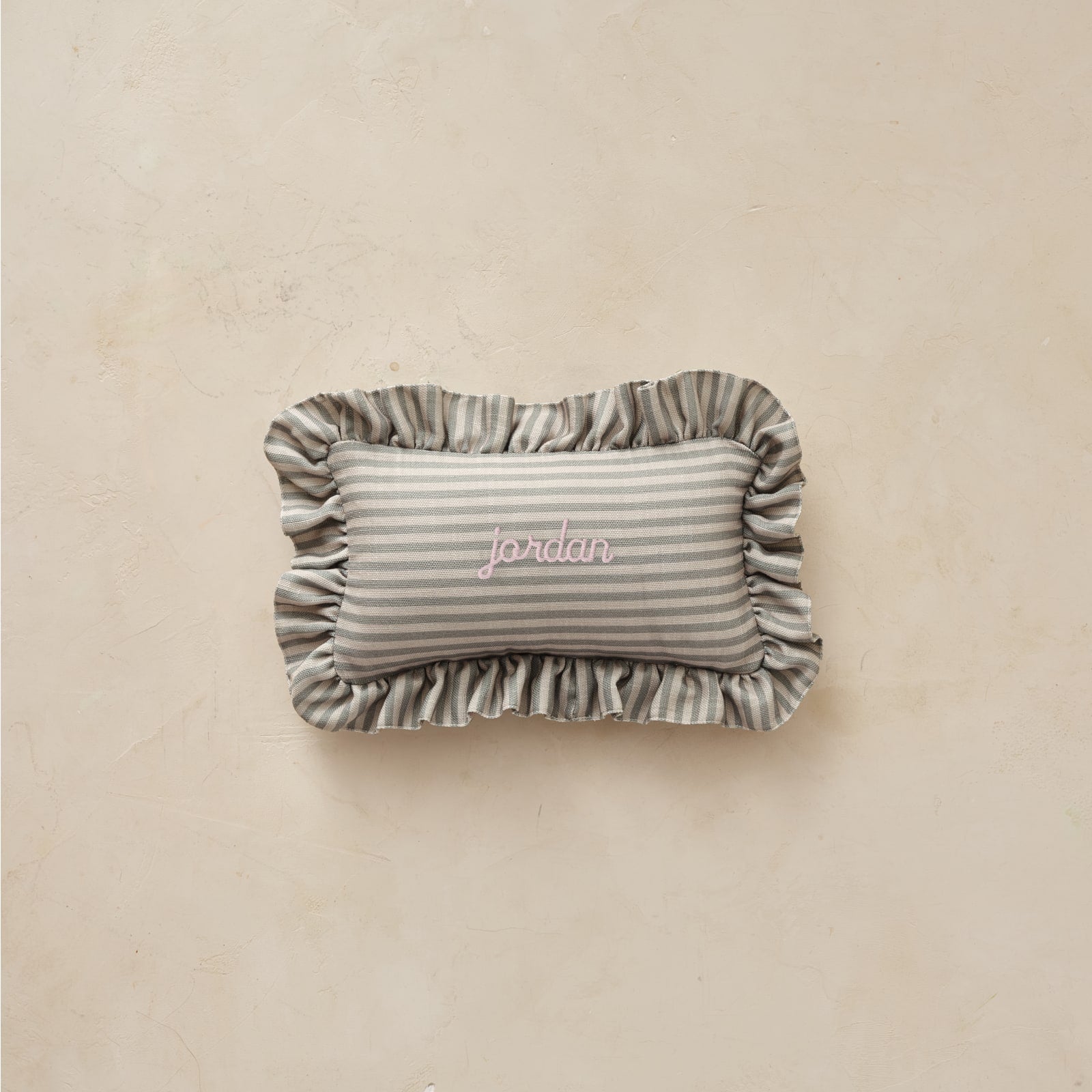 Rectangular striped pillow with ruffled edge and 'jordan' embroidery on a beige background