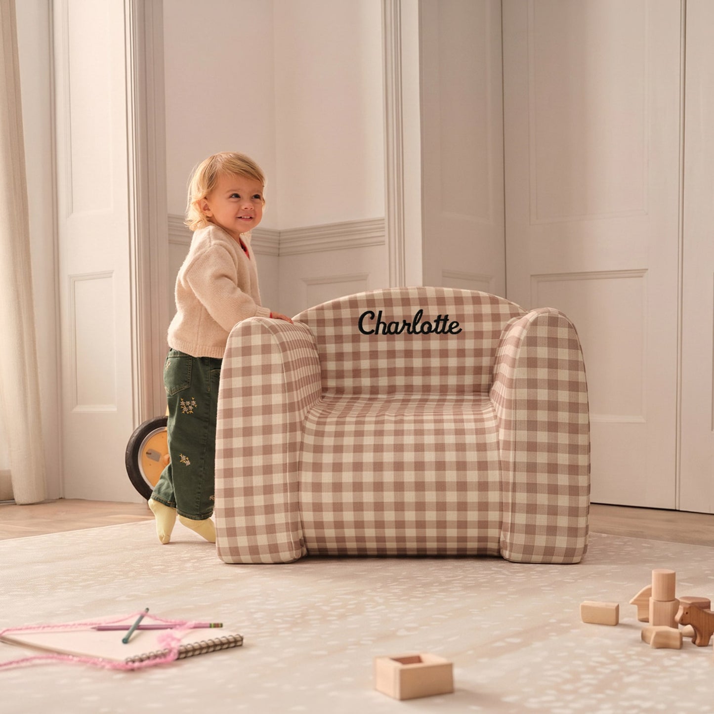 Child standing next to a gingham play chair on top of a play mat with toys