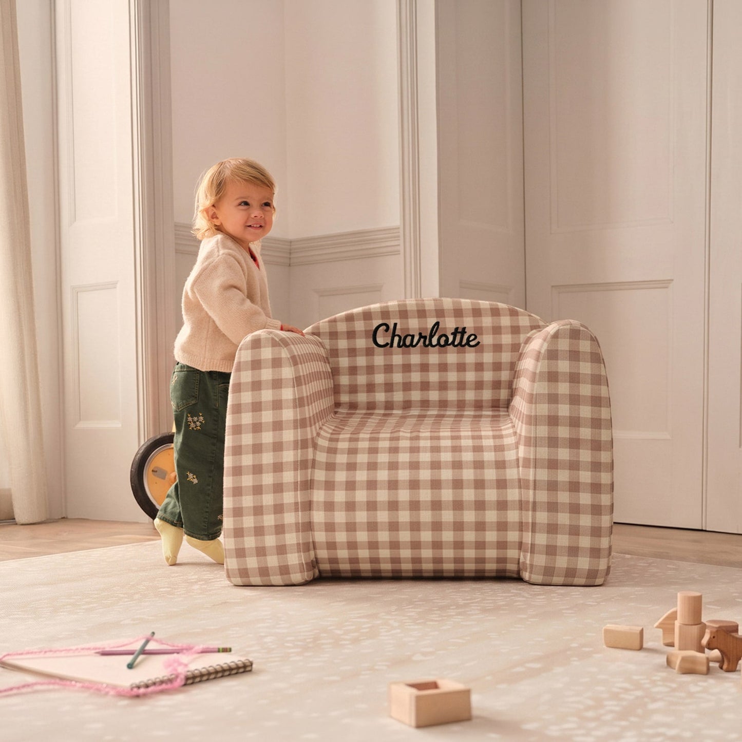 Child standing next to a gingham play chair on top of a play mat with toys