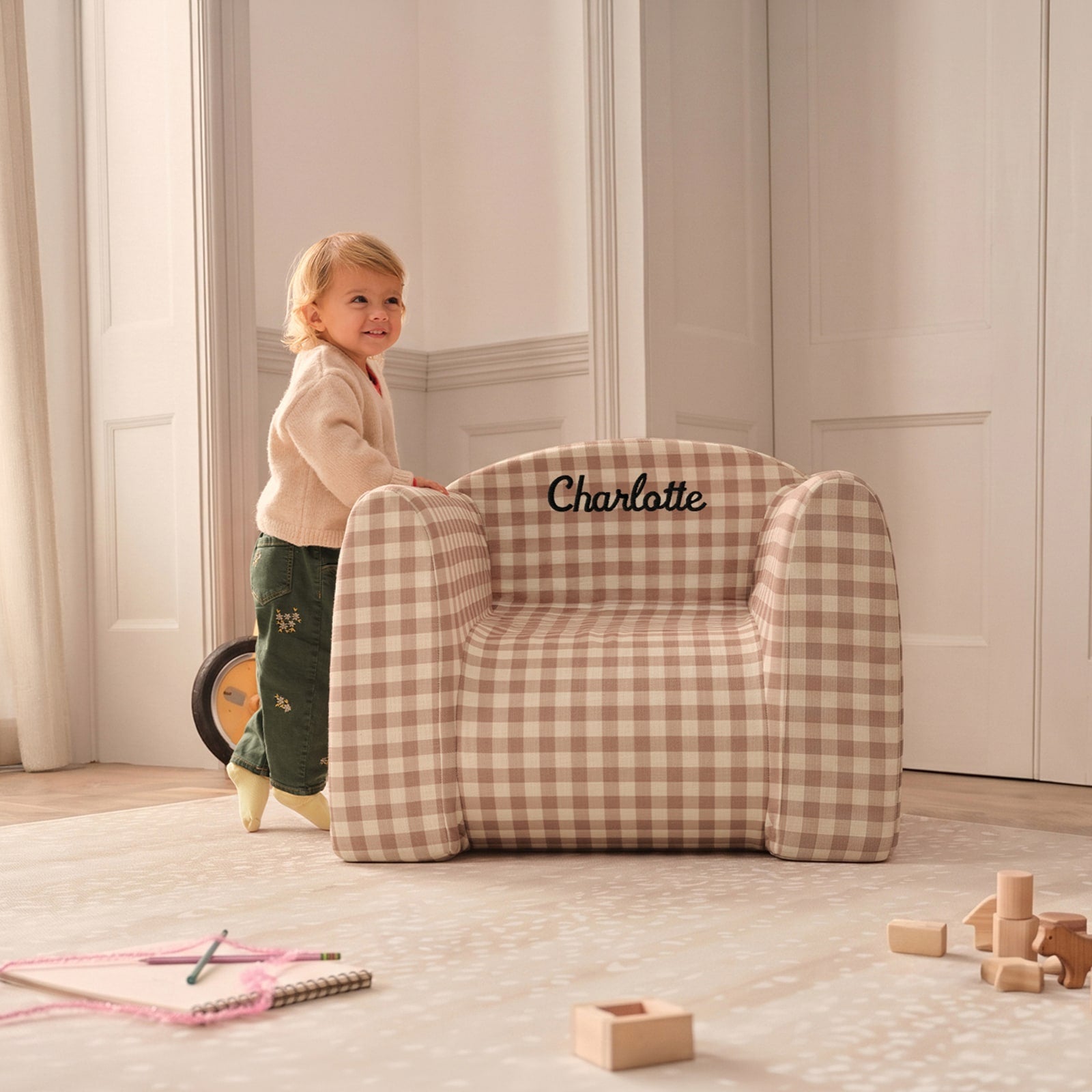 Child standing next to a gingham play chair on top of a play mat with toys