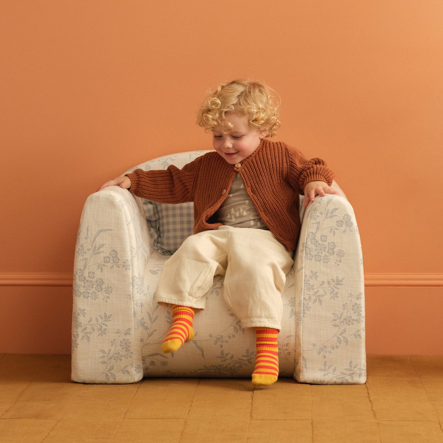 Child sitting in a blue and white floral print play chair with a ruffle pillow