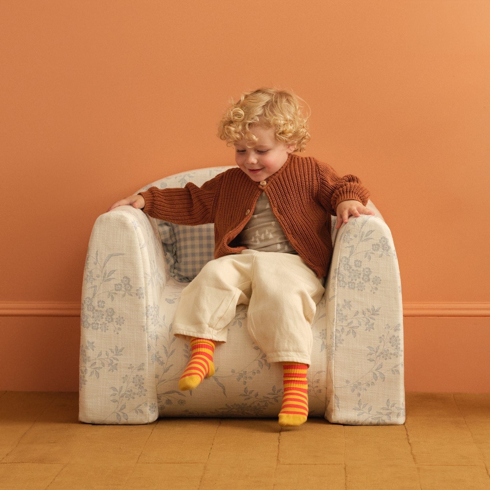 Child sitting in a blue and white floral print play chair with a ruffle pillow