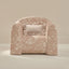 A small upholstered armchair in a dusty blush pink floral fabric, featuring a matching ruffled accent pillow, set against a warm beige studio background.
