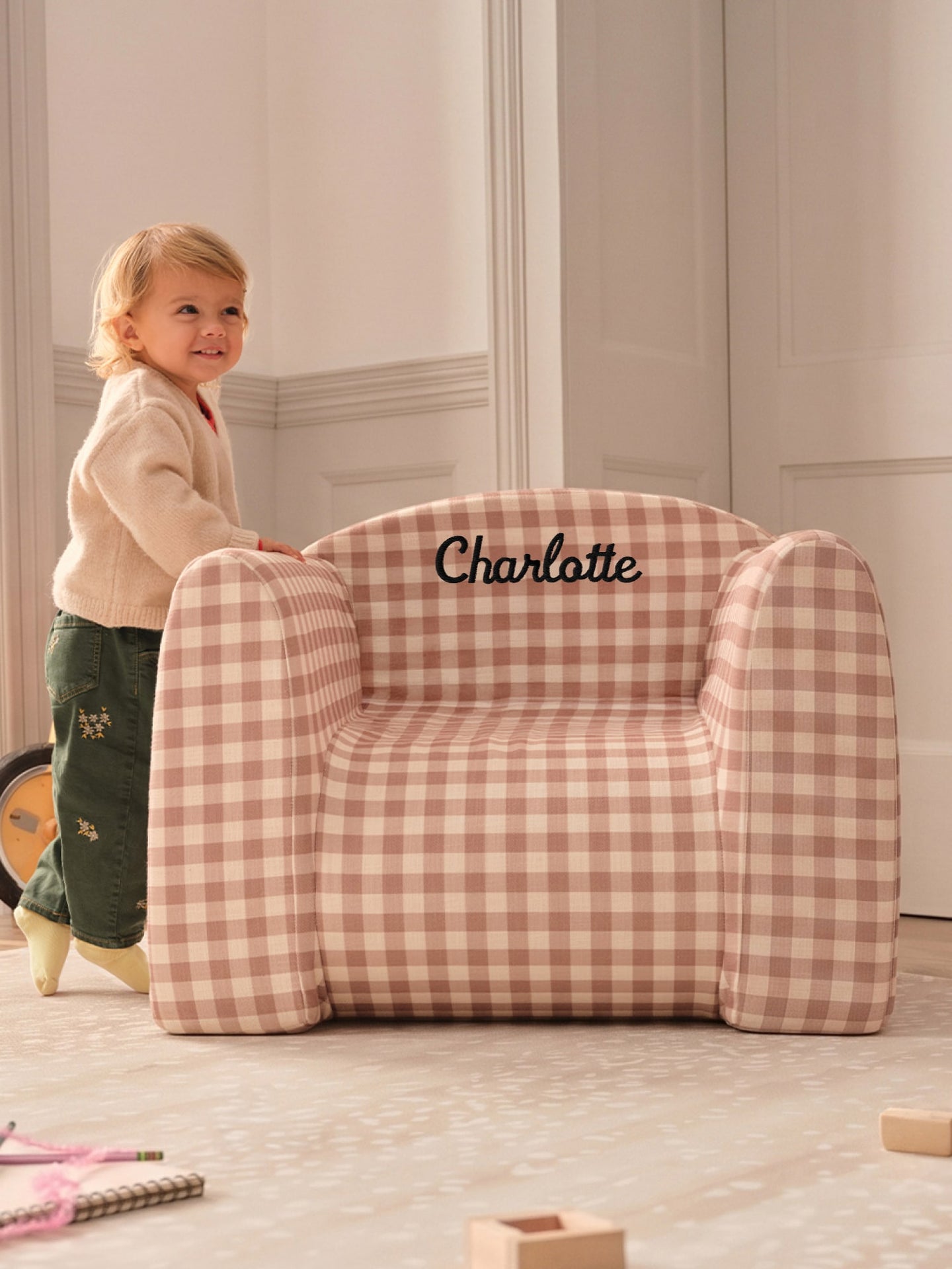 Child standing next to gingham play chair with name 'Charlotte' embroidered on it