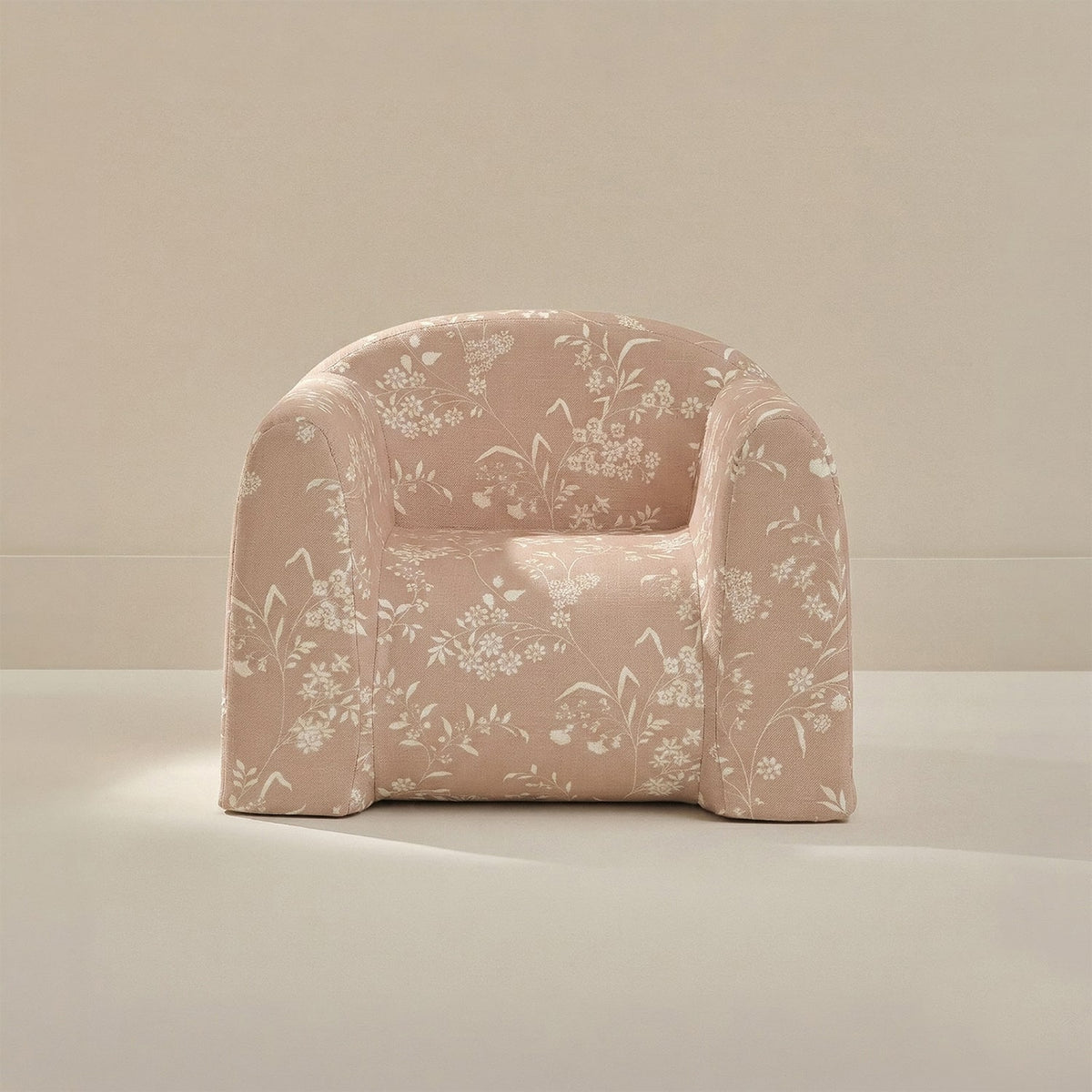 A modern low-profile armchair upholstered in a dusty pink fabric with a white floral and botanical pattern, set against a minimalist beige background.