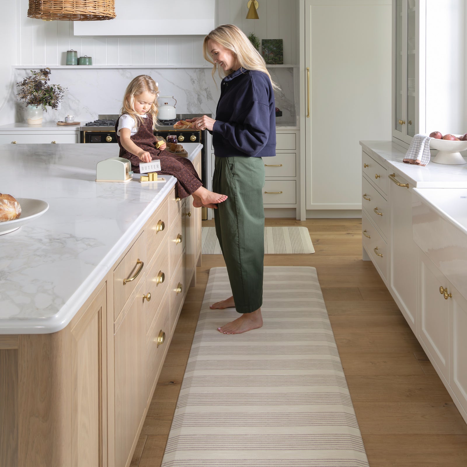 Woman and child in a modern kitchen with a long striped kitchen mat on the floor.