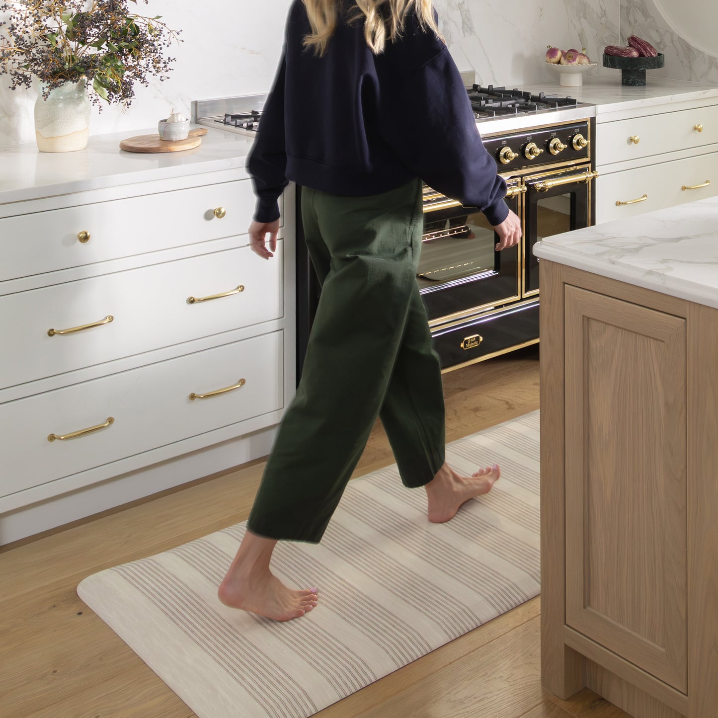 Person walking on a striped rug in a kitchen with white cabinets and a black stove.