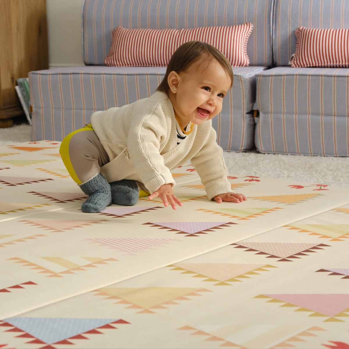 Smiling baby crawling on the Sylvia Kaleidoscope tumbling mat in a living room