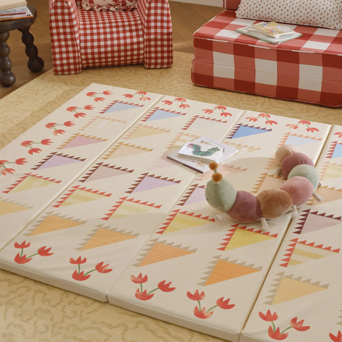 Sylvia Kaleidoscope tumbling mat unfolded on a rug with a book and plush caterpillar toy
