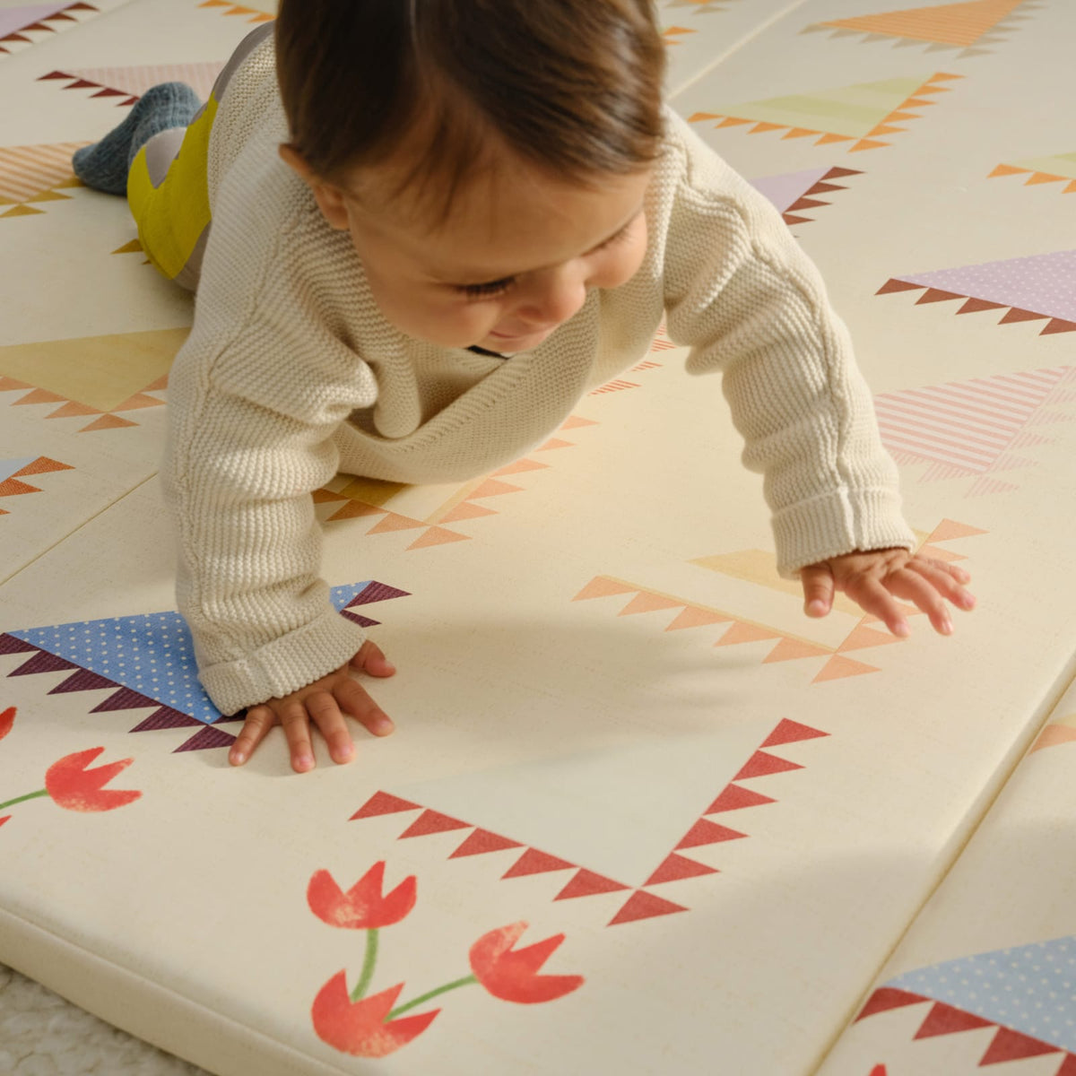 Close-up of a baby crawling on the Sylvia Kaleidoscope tumbling mat with red tulip details