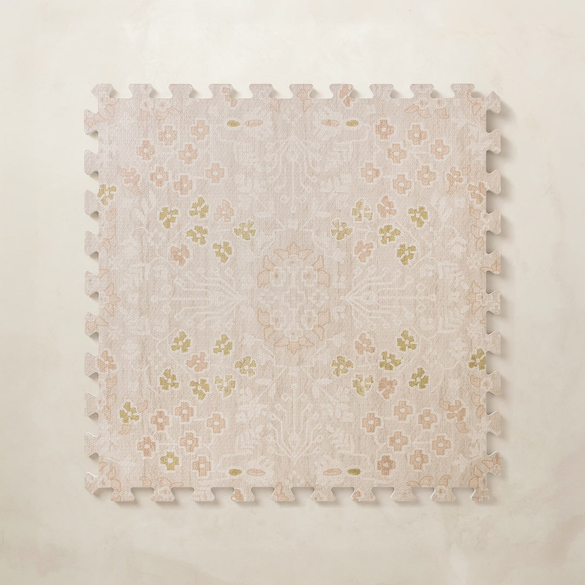 A square interlocking foam play mat tile with a faded blush and cream floral medallion pattern, shown from above on a light beige background.