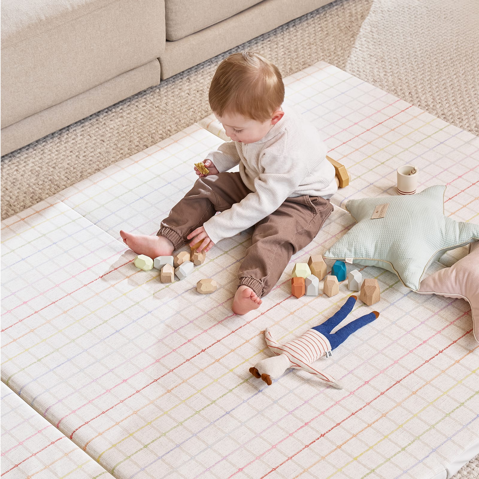 Child playing on a colorful mat with toys in a living room setting