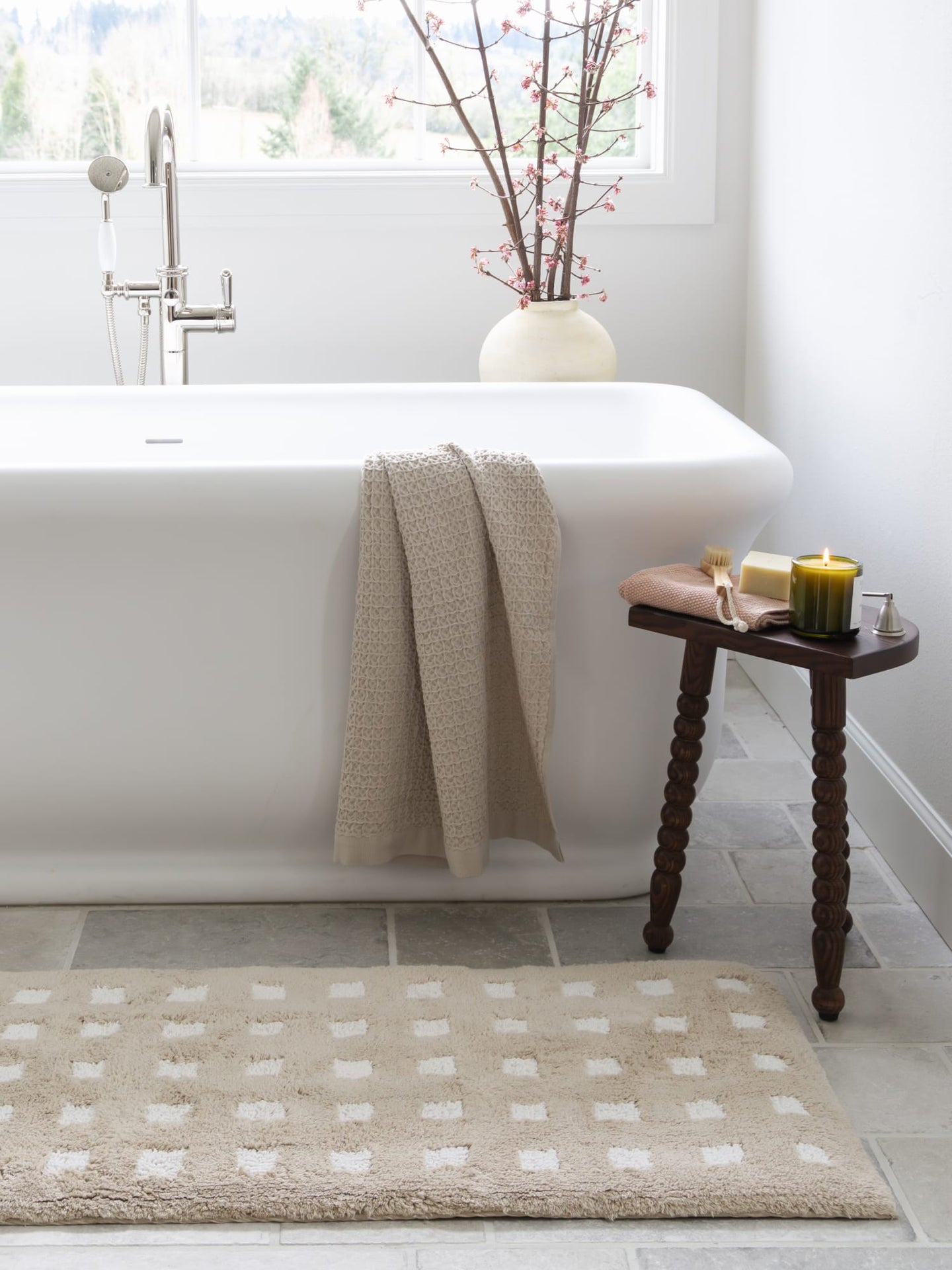 Bathroom with a white bathtub, towel, beige bath rug, and small table with candles.